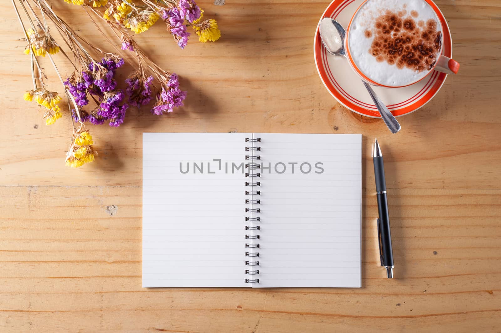 Opened notebook with blank area for text or message, pen and a cup of hot coffee on wood table in afternoon time