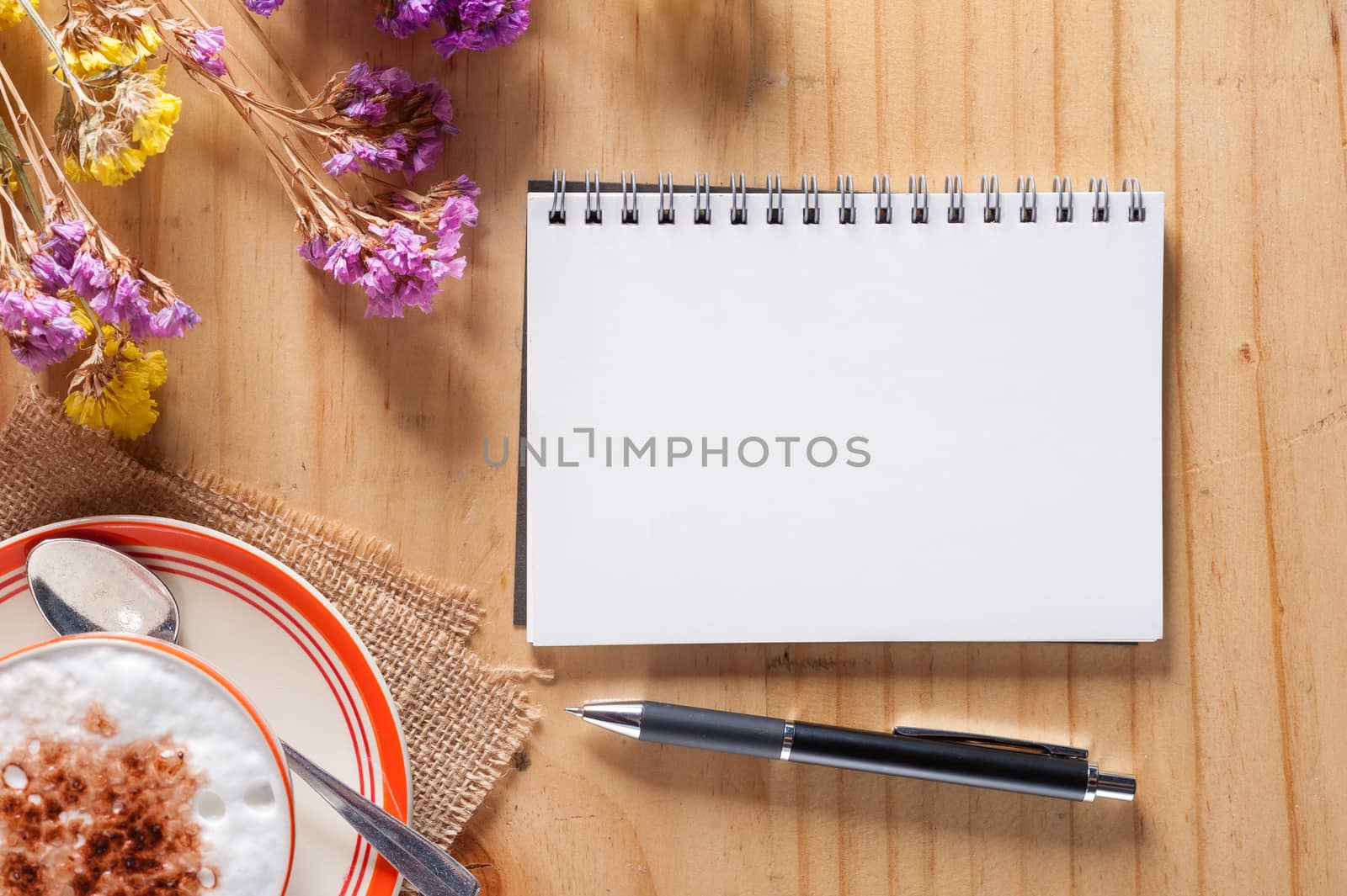 Opened notebook with blank area for text or message, pen and a cup of hot coffee on wood table in afternoon time