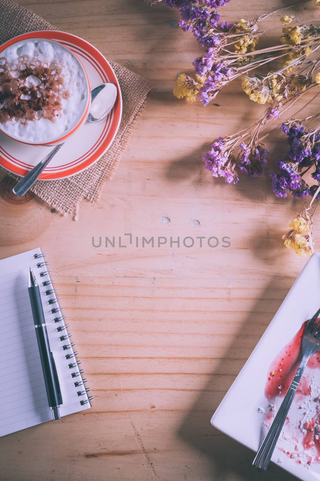 Wood table background with blank area for text or message, opened notebook, pen and a cup of hot coffee as frame in afternoon time with film filter effect