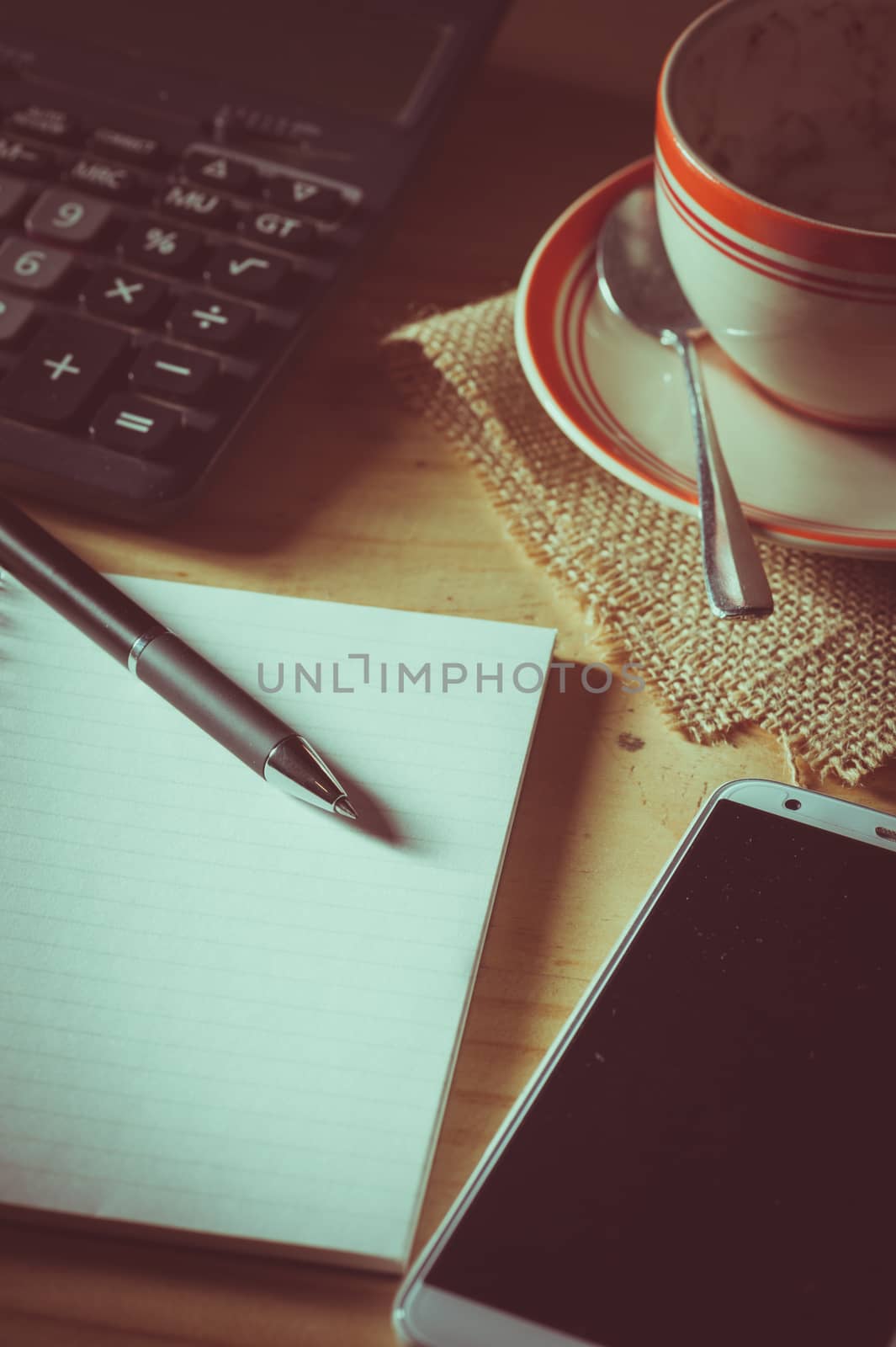 Opened notepad, pen, smart phone, and calculator on wood table in evening time with low key scene and film filter effect