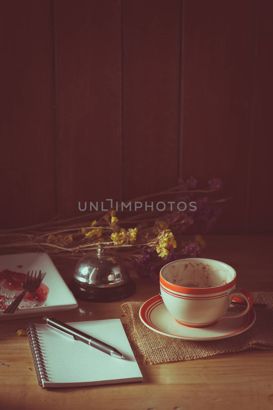Opened notepad, pen, and a cup of hot coffee on wood table in morning time with low key scene and film filter effect
