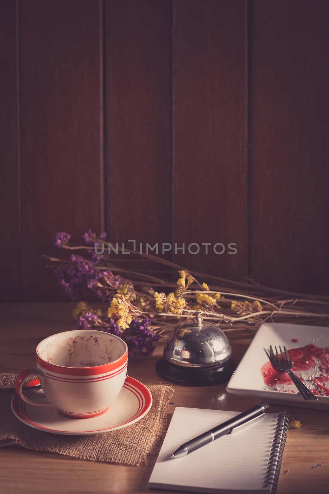 Opened notepad, pen, and a cup of hot coffee on wood table in morning time with low key scene and film filter effect