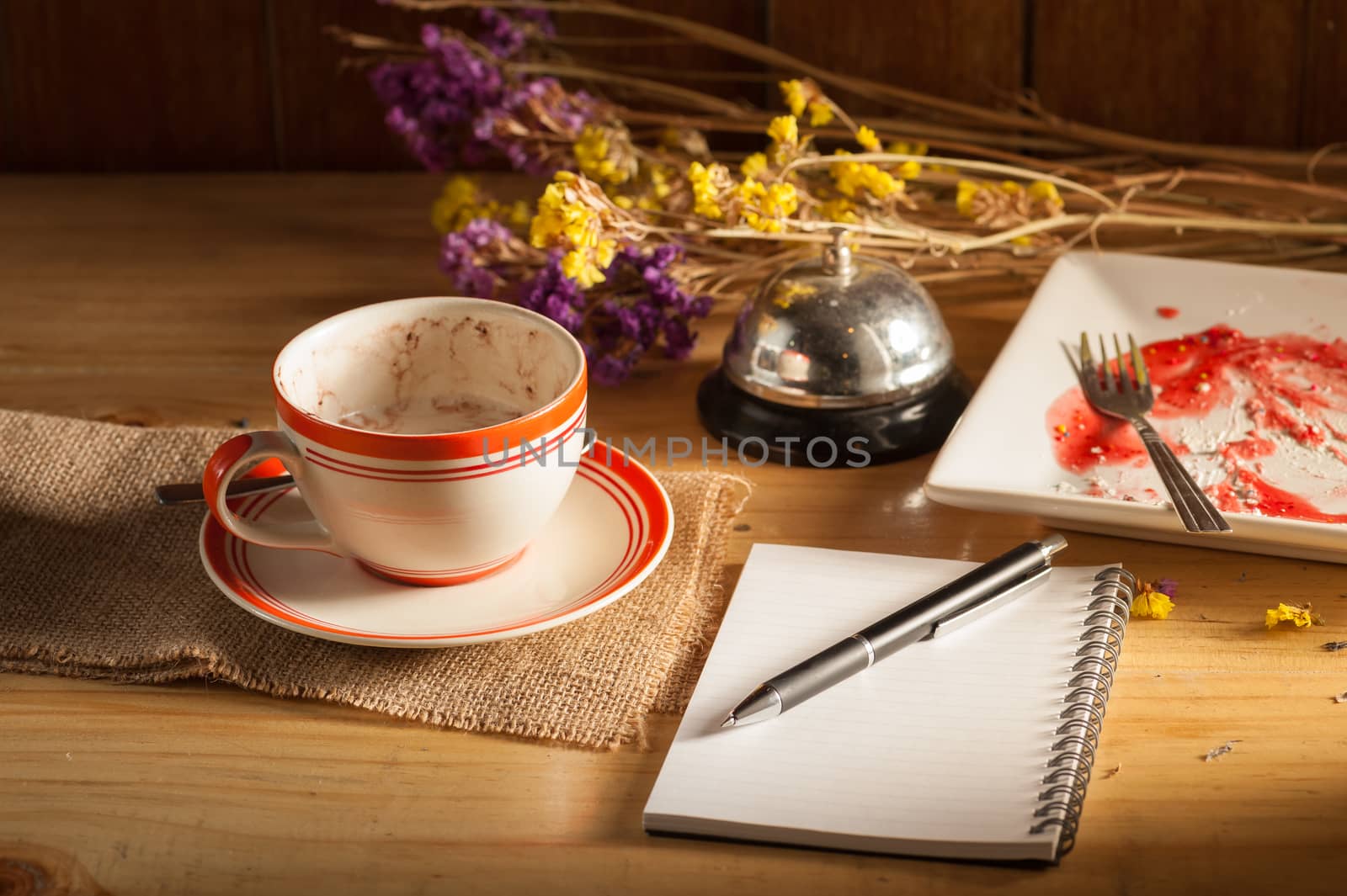 Opened notepad, pen, smart phone, and a cup of hot coffee on wood table in morning time with low key scene