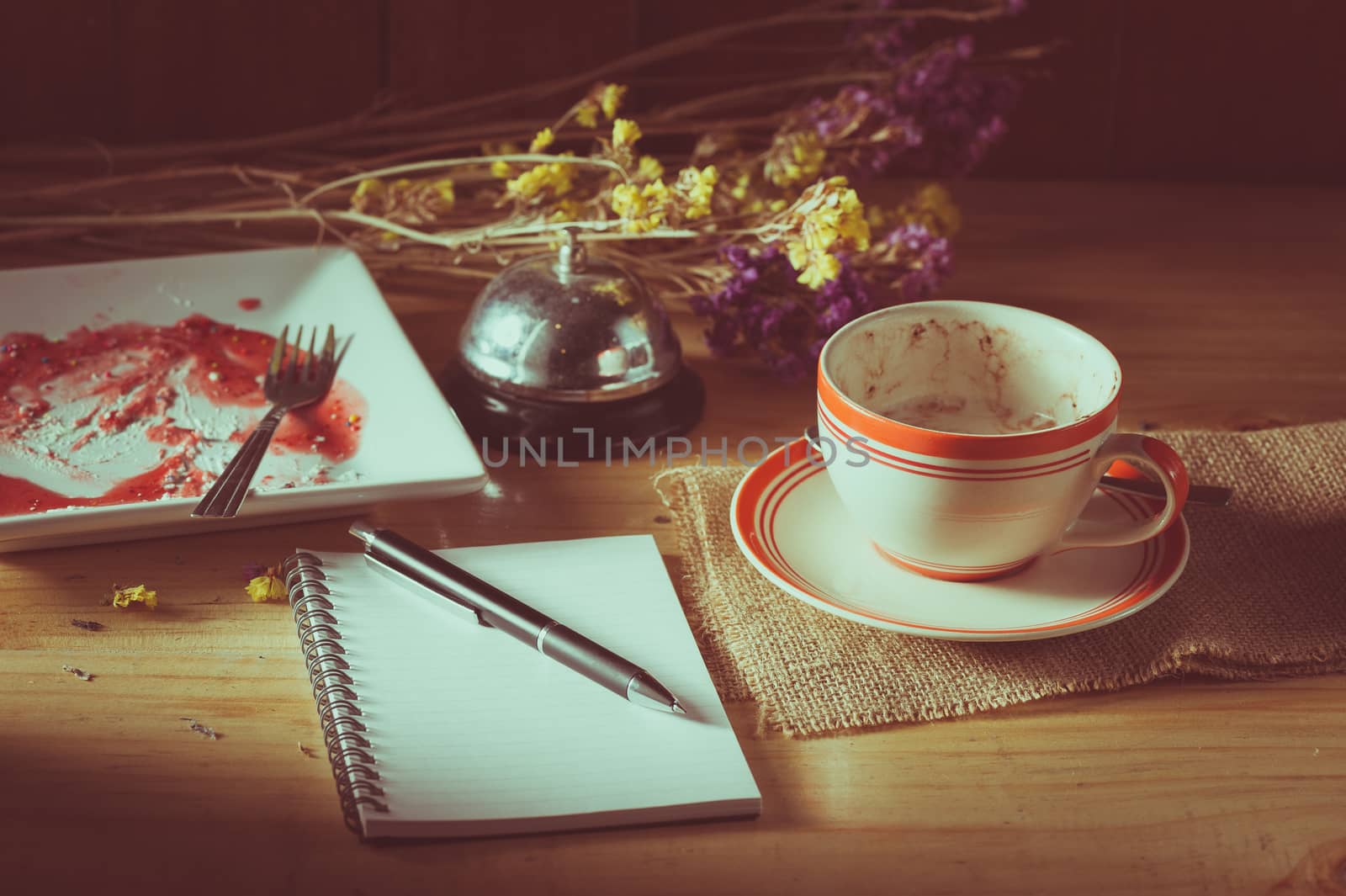 Opened notepad, pen, and a cup of hot coffee on wood table in morning time with low key scene and film filter effect