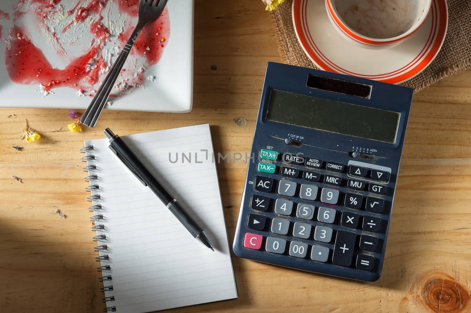 Opened notepad, pen, and calculator on wood table in evening time with low key scene