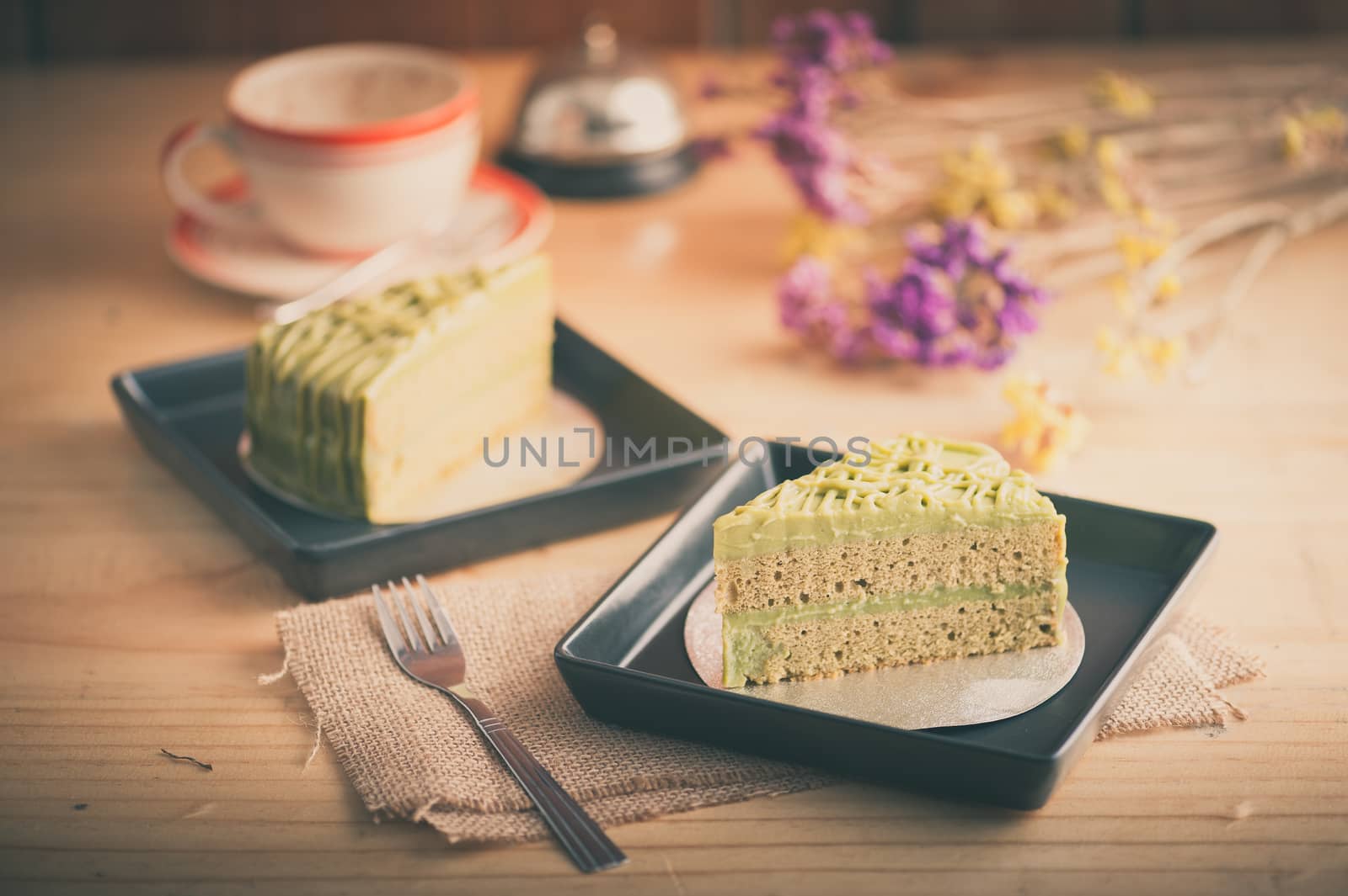Green tea cake in black ceramic dish on wood table in afternoon time with film filter effect