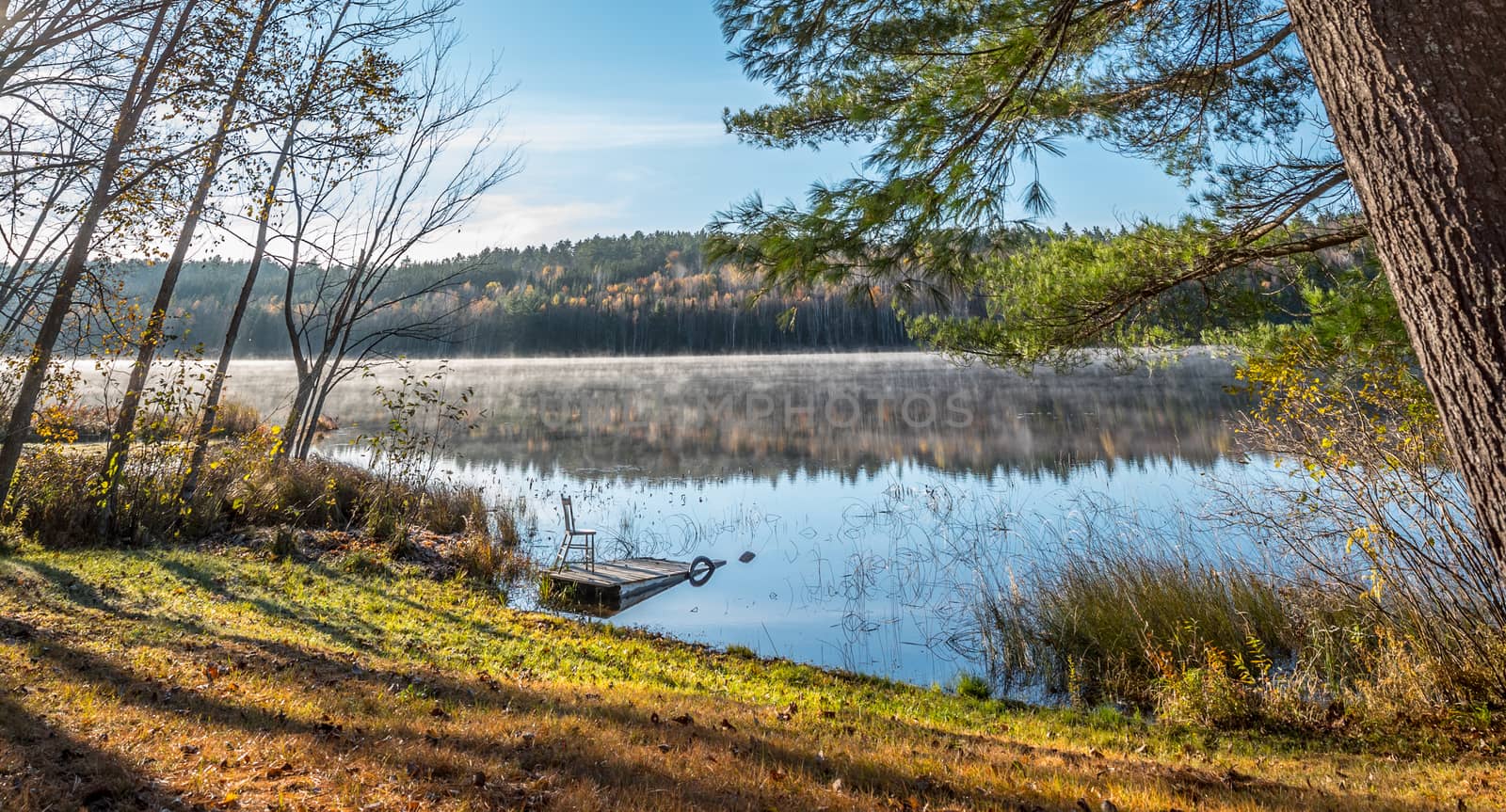 Morning sun rise revealing light fog.  Chair sits on a partially submerged dock beside a lake in Ontario, Canada.