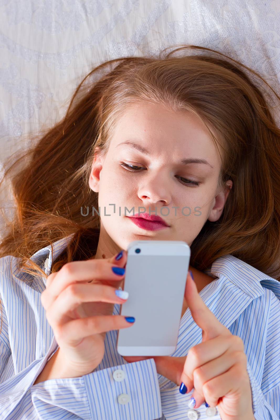 woman sending text with a mobile phone in bed by victosha