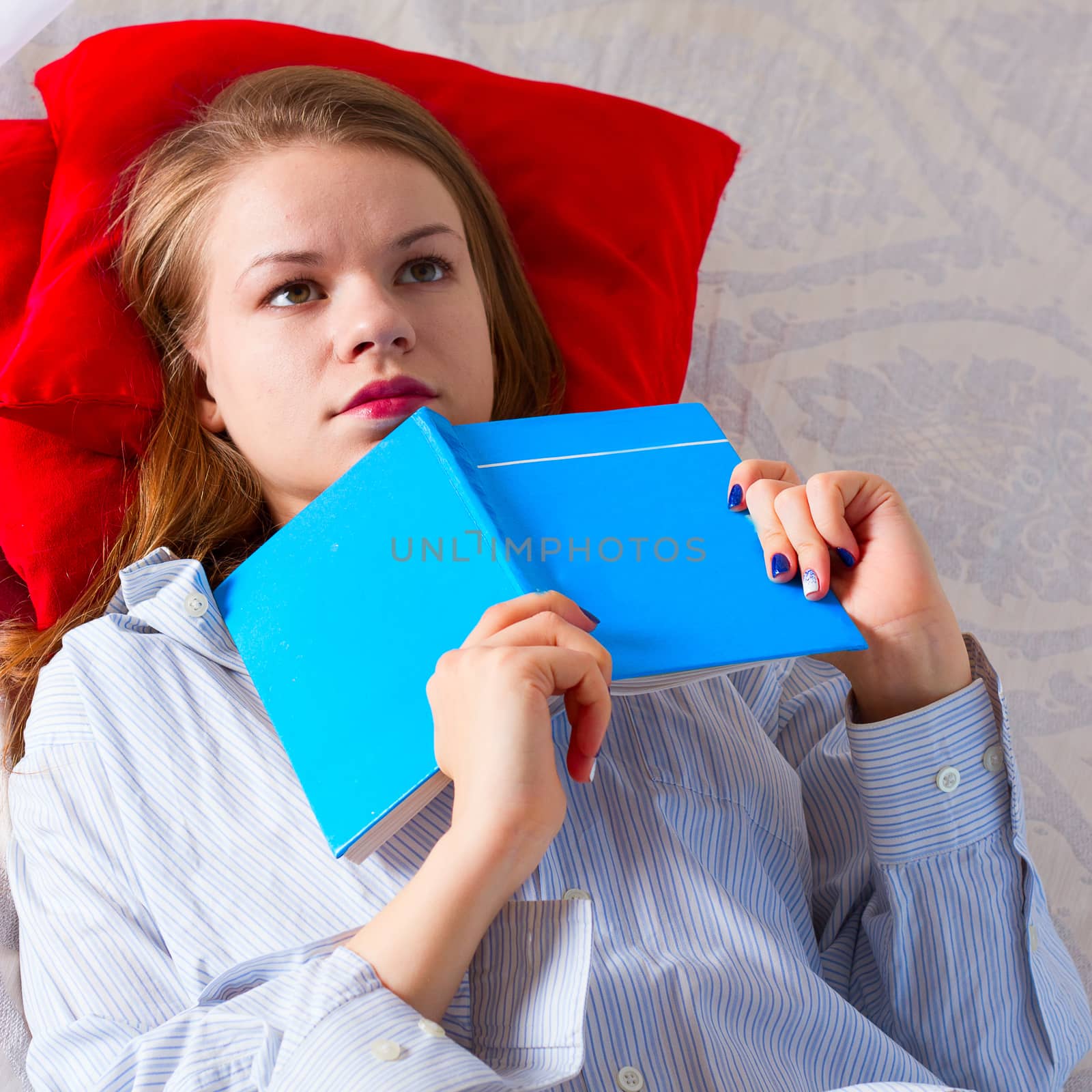 The girl in a man's shirt is reading a book in bed