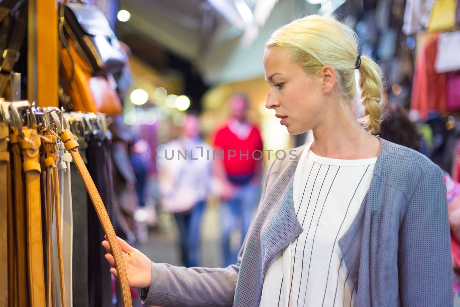 Beautiful casually dressed caucasian blond woman shopping for new leather belt on crafts market in Chania, Crete, Greece.