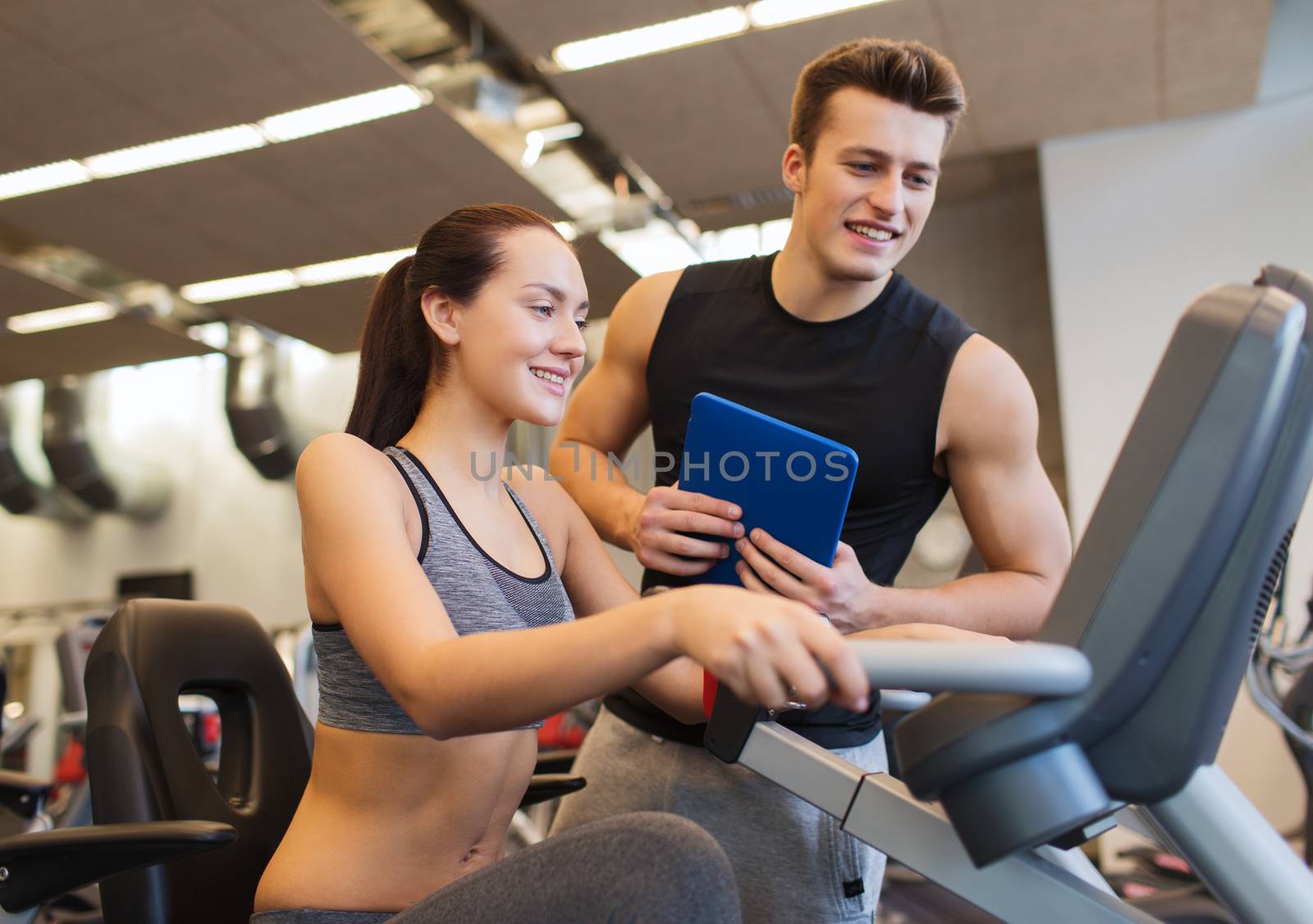 happy woman with trainer on exercise bike in gym by dolgachov