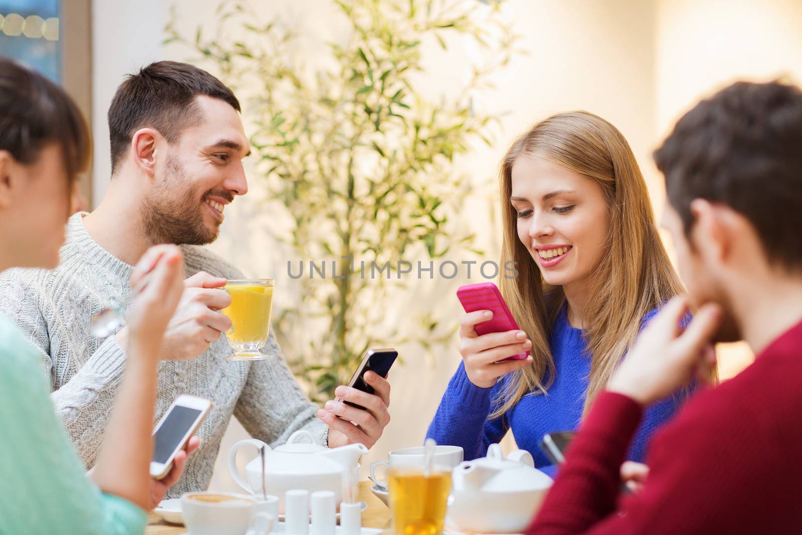 people, leisure, friendship and technology concept - group of happy friends with smartphones meeting at cafe and drinking tea