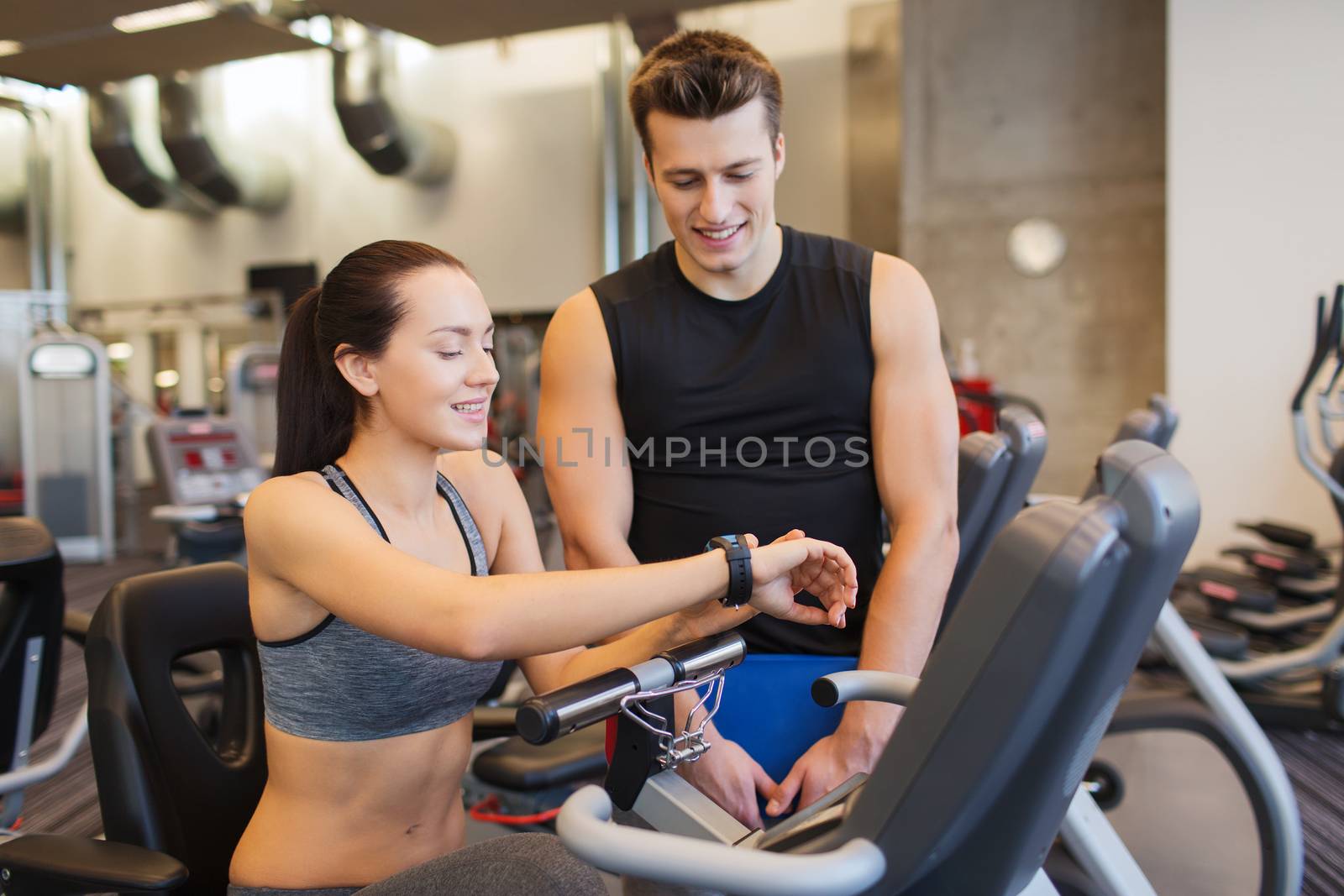 happy woman with trainer on exercise bike in gym by dolgachov