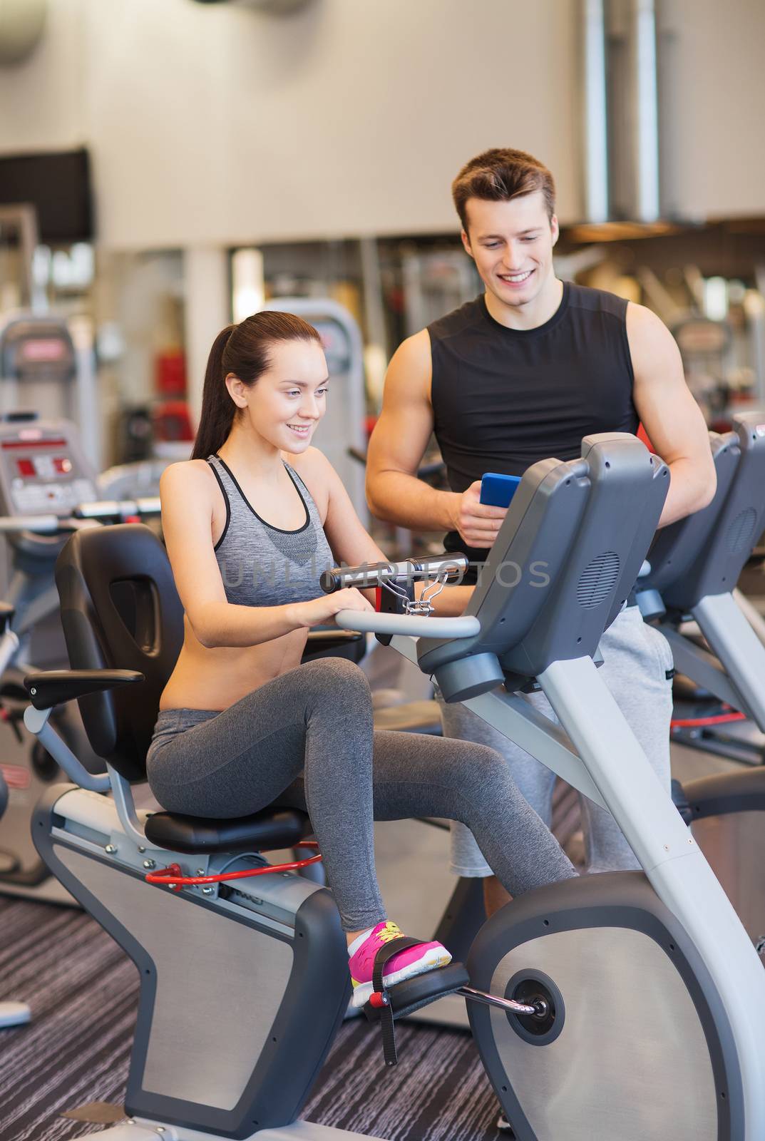 happy woman with trainer on exercise bike in gym by dolgachov