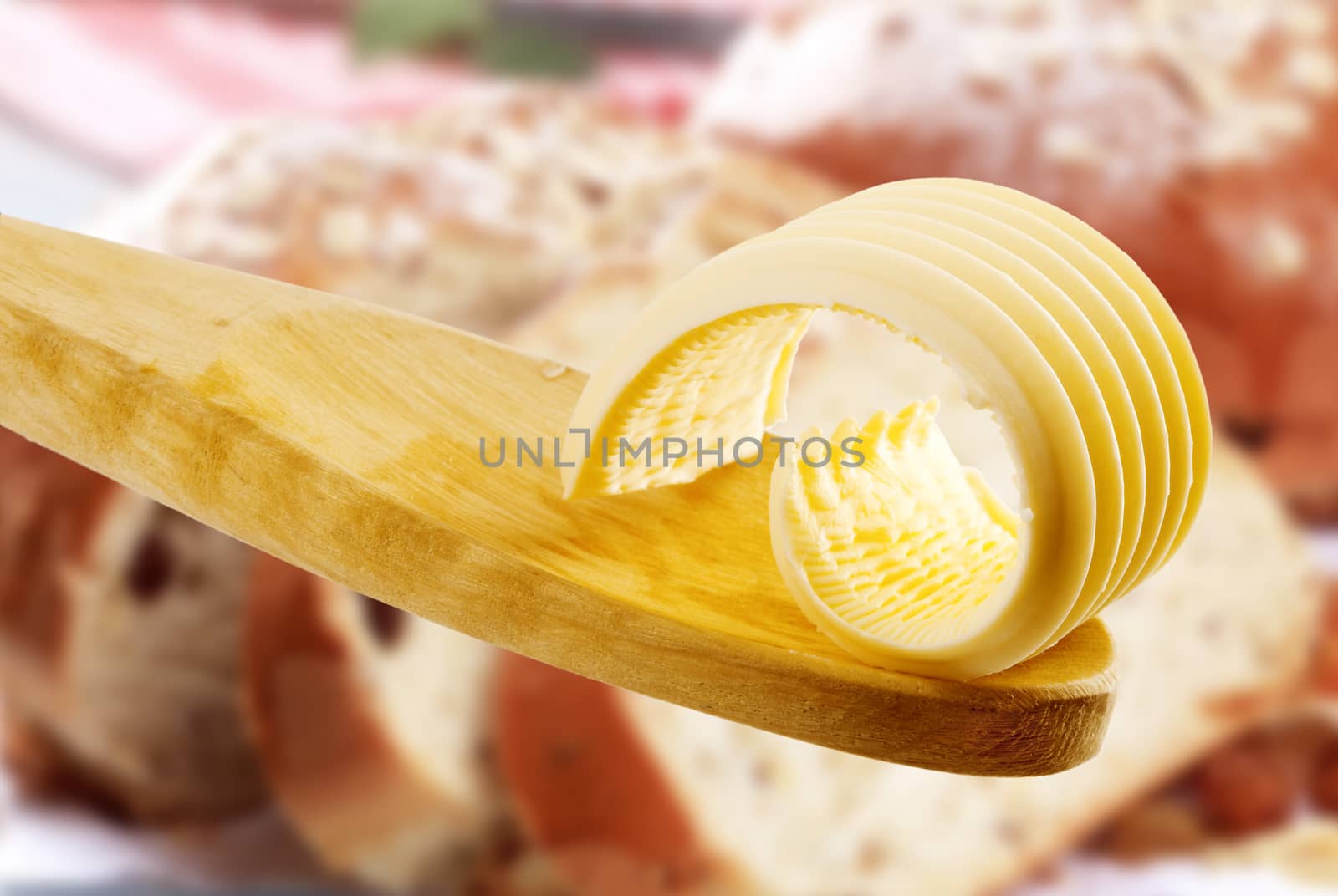 Butter curl on a wooden spoon, baked products in the background