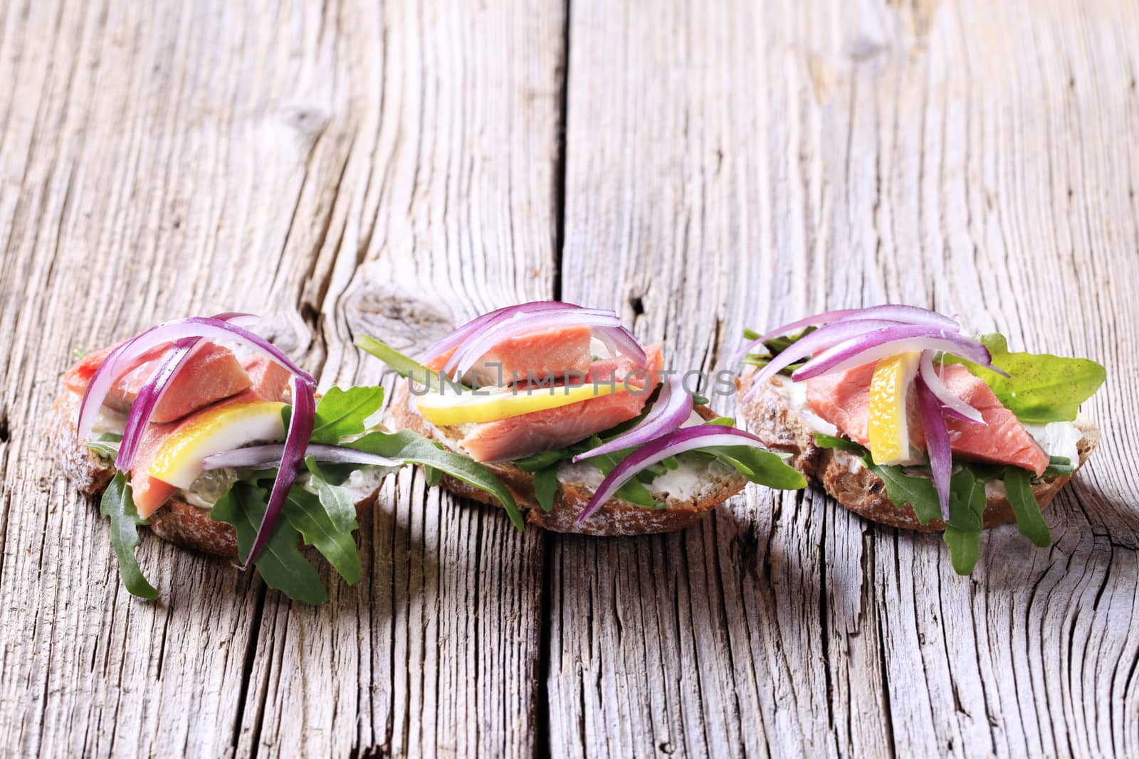 Salmon open faced sandwiches garnished with red onion and lemon