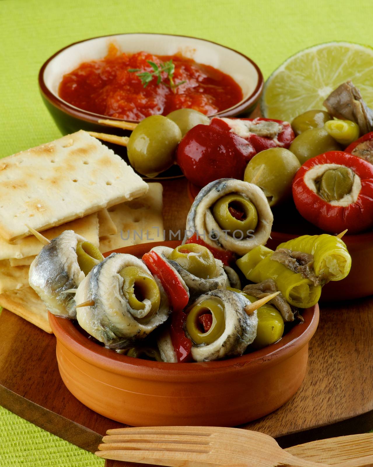 Delicious Spanish Snacks with Anchovies, Green Olives, Stuffed Small Peppers, Bread Sticks and Tomatoes Sauce in Various Bowls closeup on Green Napkin