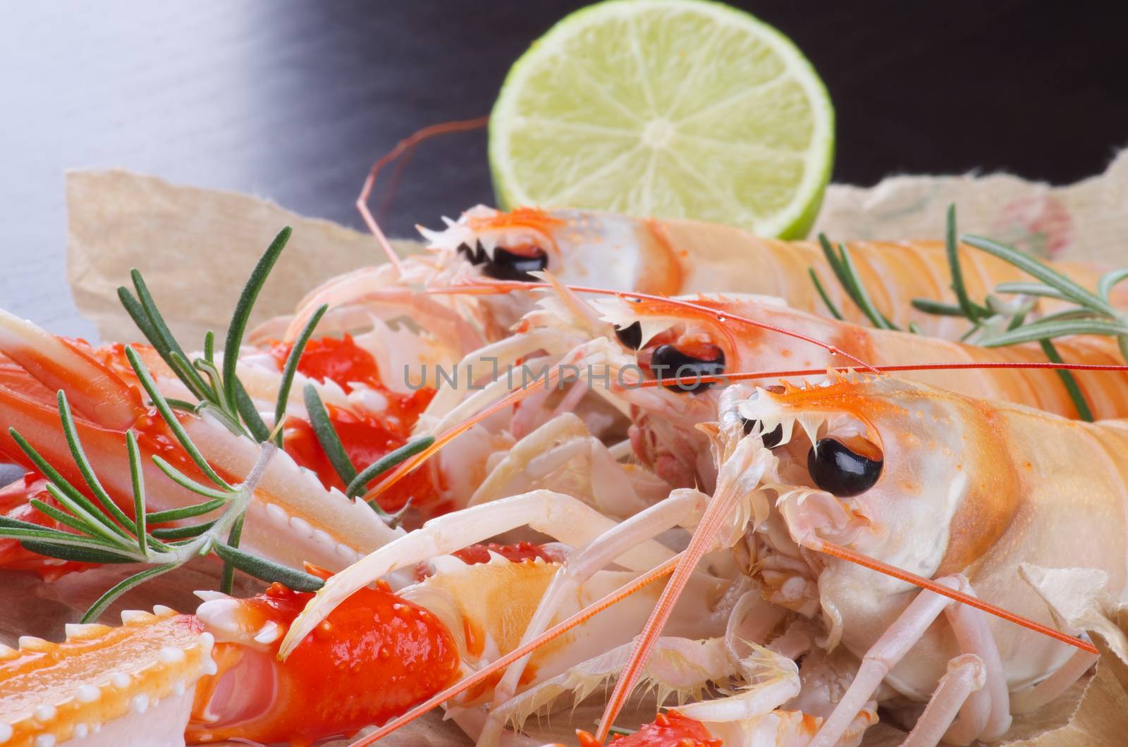 Three Delicious Grilled Langoustines with Lime and Rosemary closeup on Dark Wooden background. Focus on Foreground