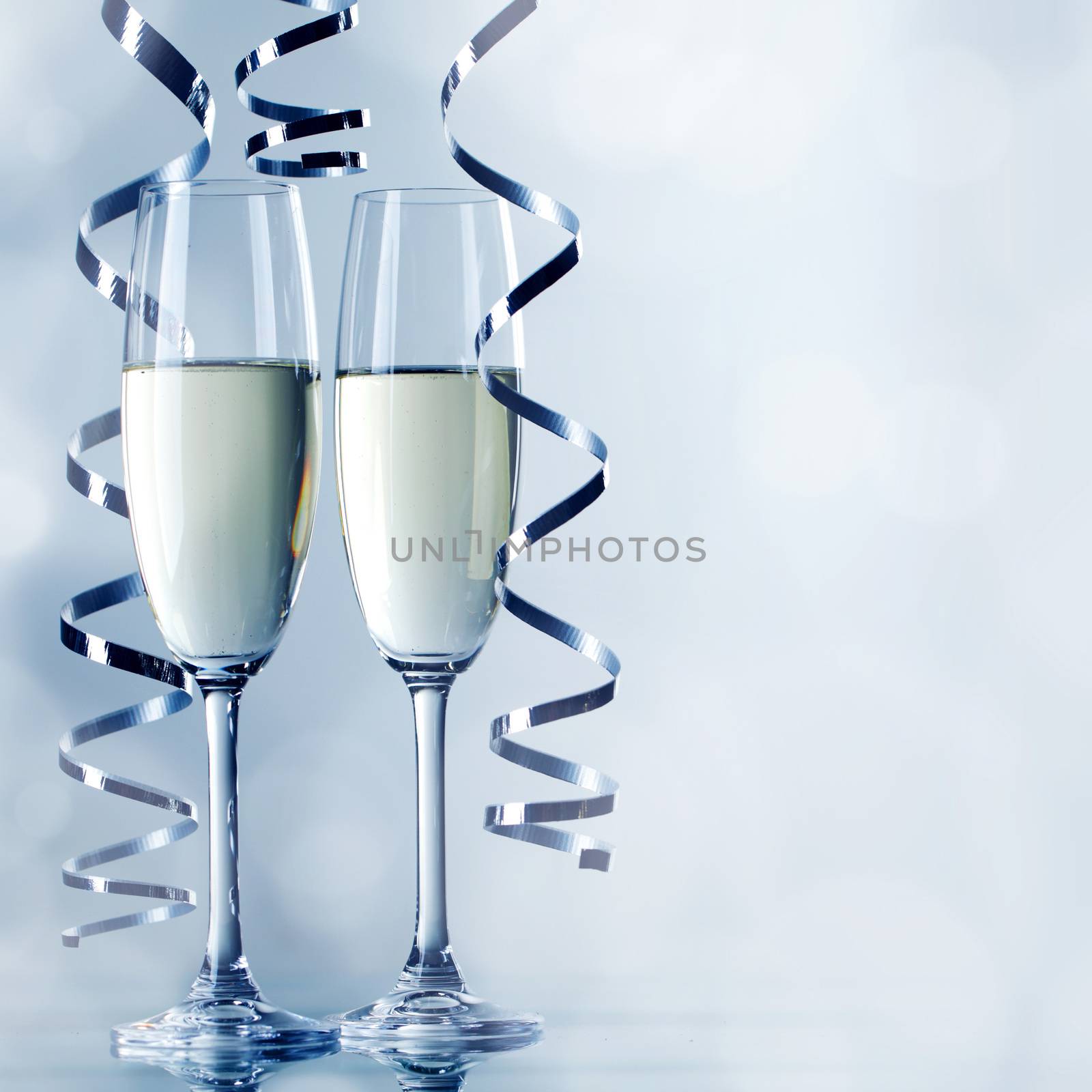 Two glasses of champagne and ribbons on light bokeh background