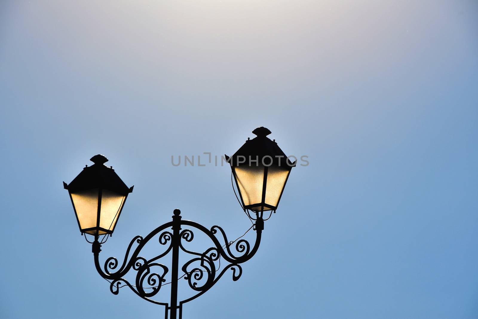 Street antique style double lamp post with effect of shine at late day blue sky background