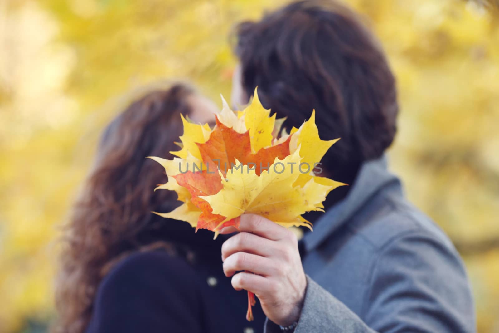 Beautiful couple with maple leaves kissing in autumn park