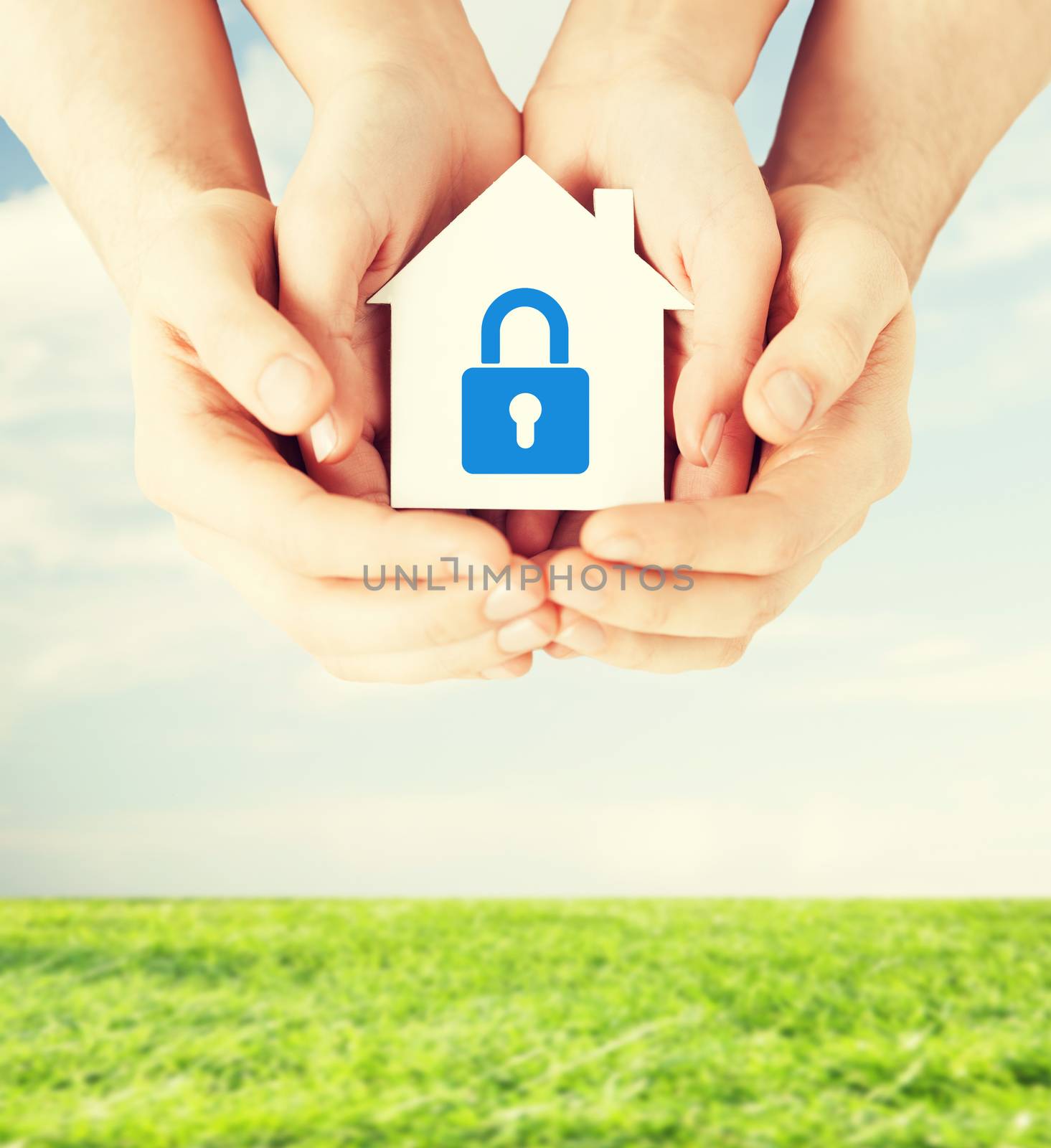 real estate and family home security concept - closeup picture of male and female hands holding white paper house with blue lock