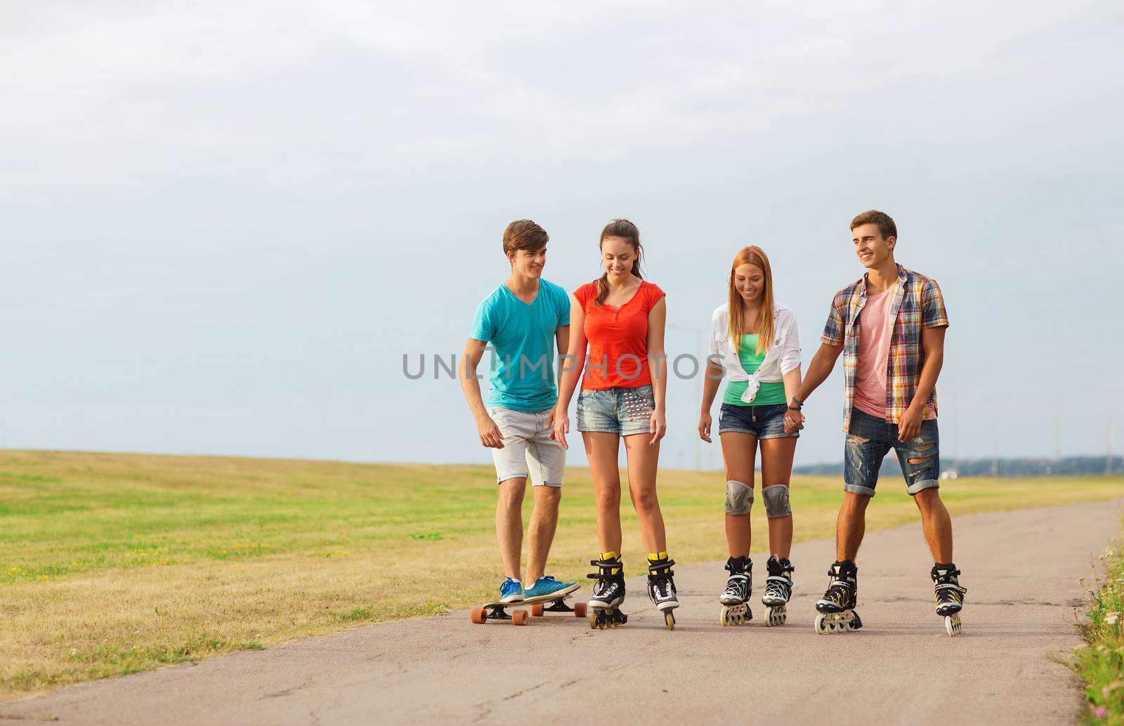 holidays, vacation, love and friendship concept - group of smiling teenagers with roller skates and skateboard riding outdoors