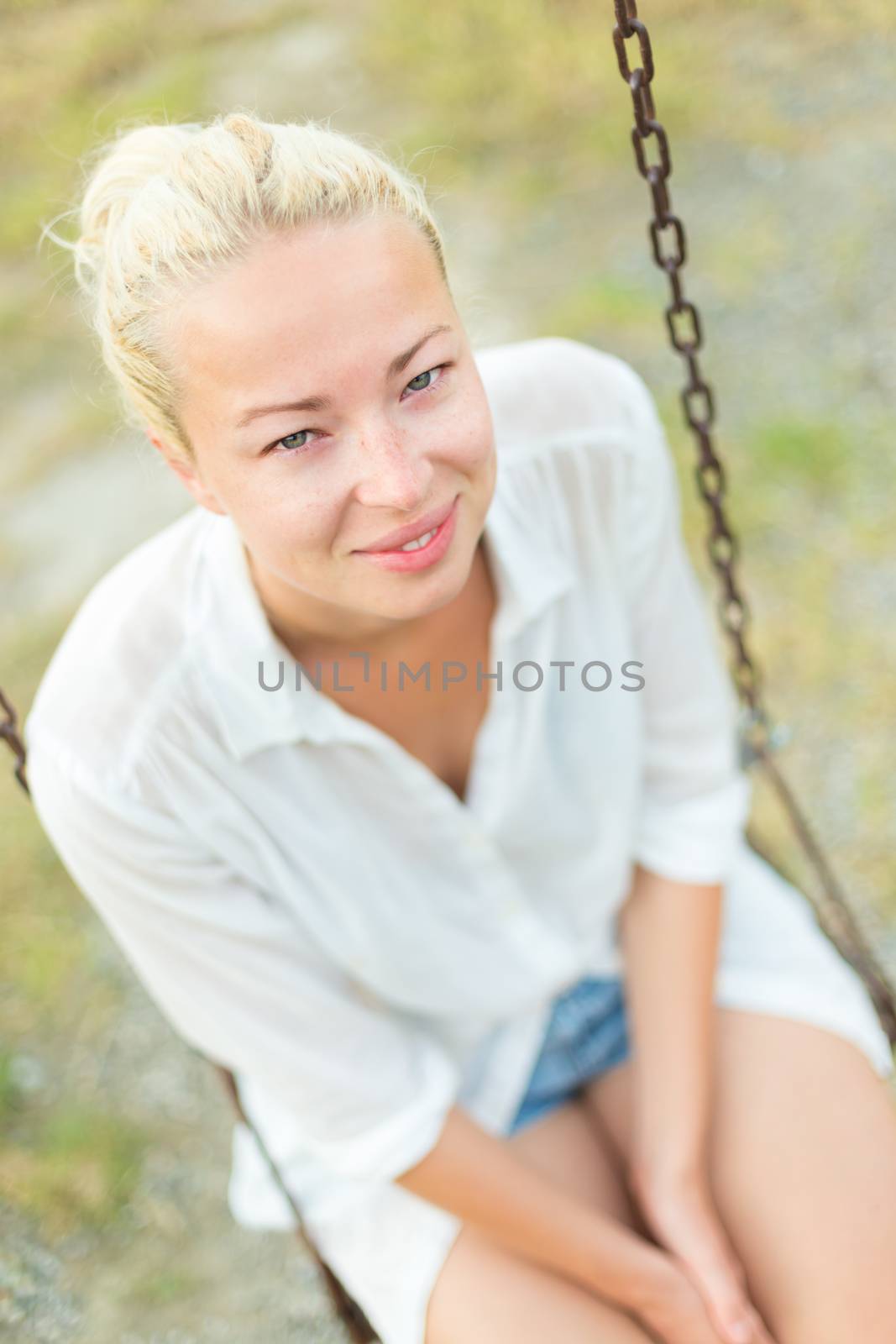 Young blonde woman sitting on the swing in park.