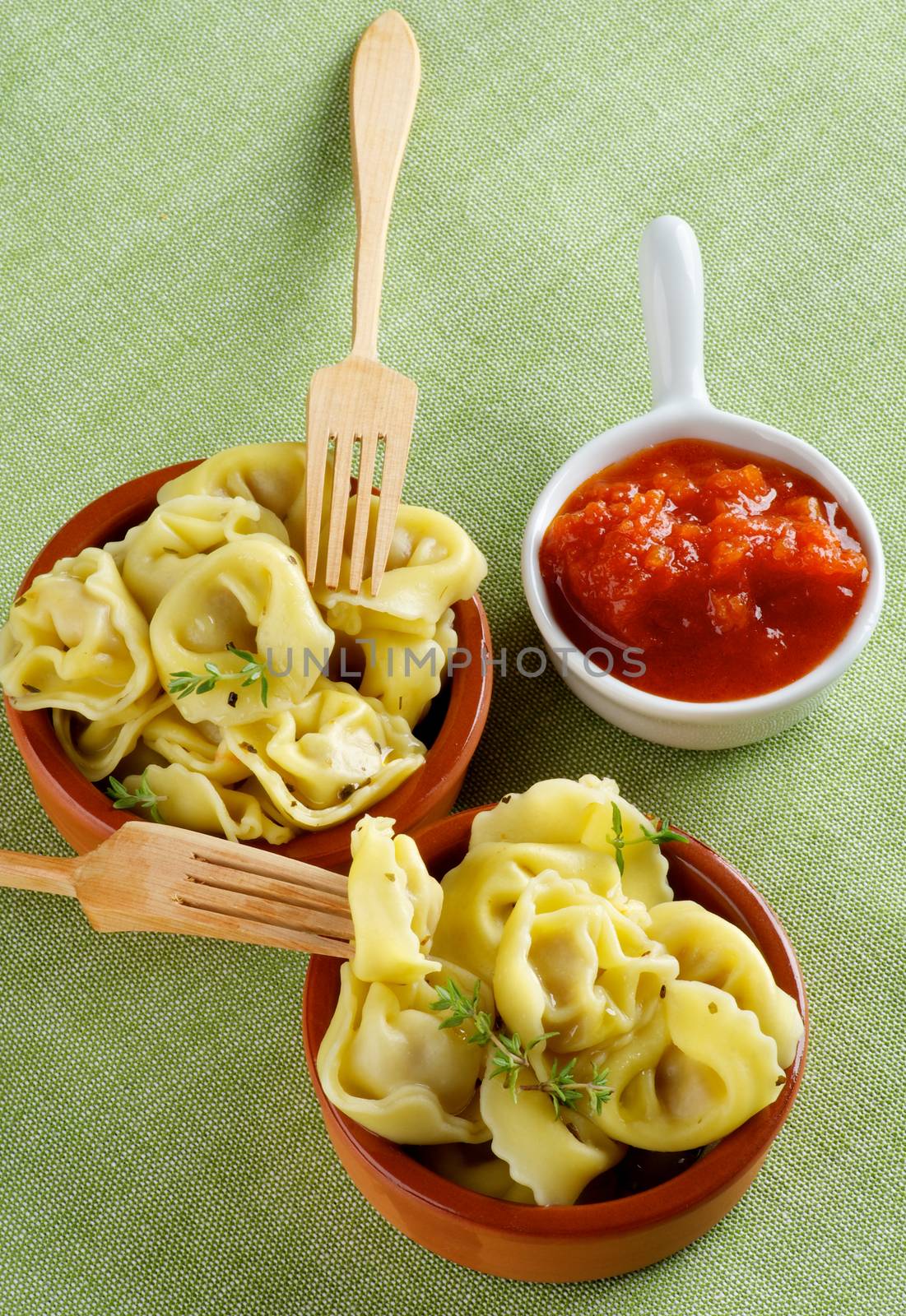 Delicious Meat Cappelletti in Ceramic Bowls with Tomatoes Sauce and Wooden Forks closeup on Green Napkin background