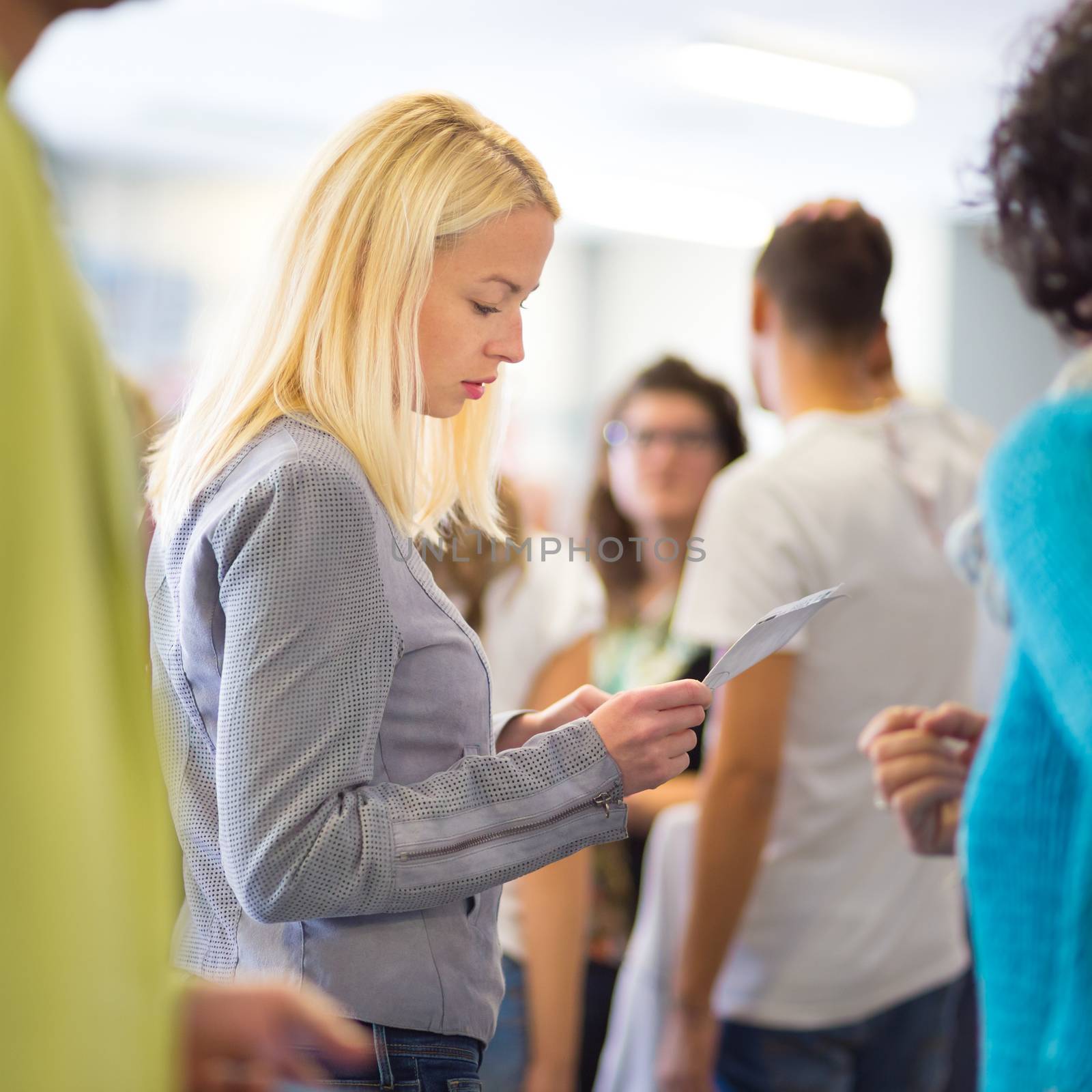 Young blond caucsian woman waiting in line with plain ticket in her hands. Lady standing in a long queue to board a plane.