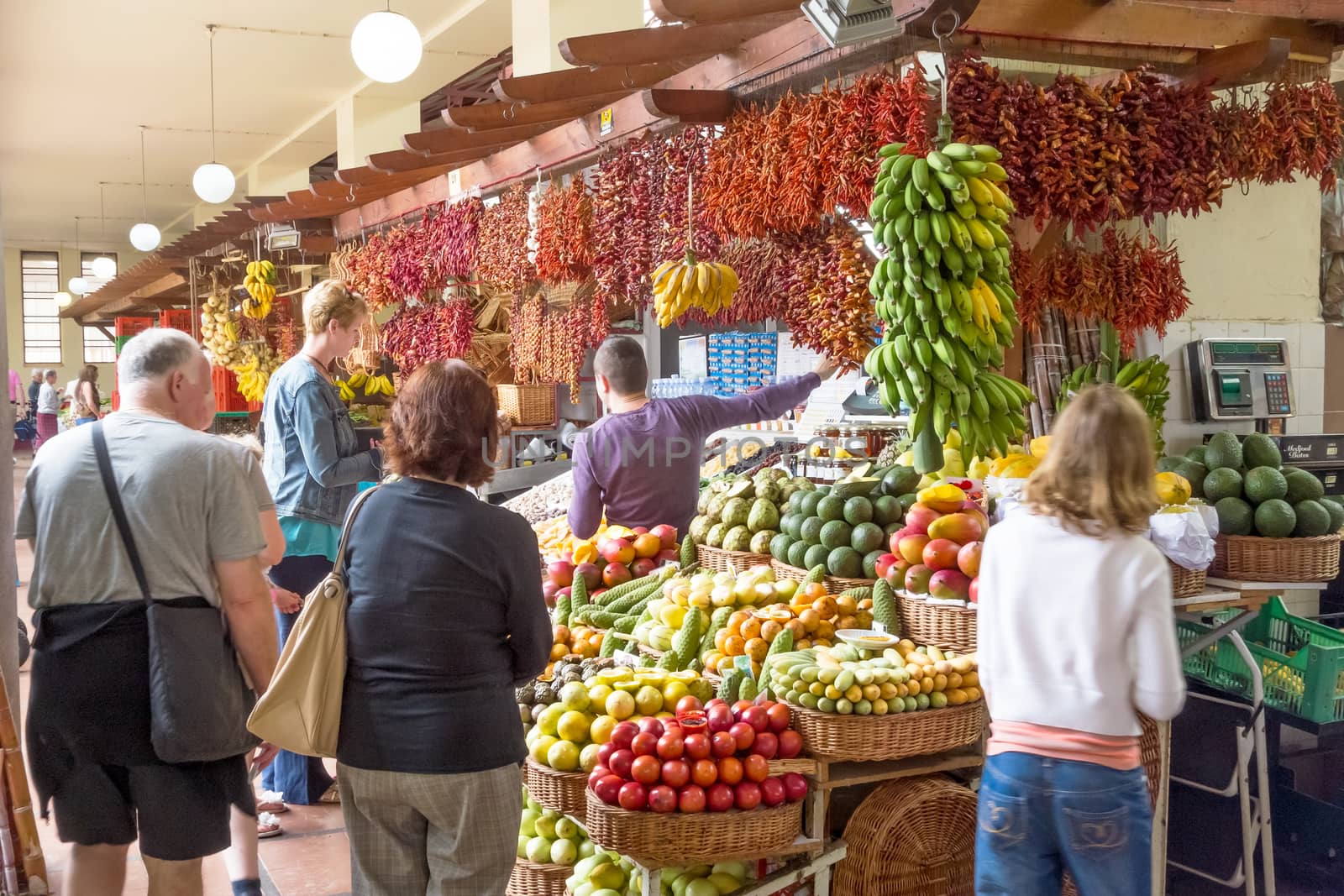 Funchal, Portugal - June 3, 2013: Market in Funchal, Madeira. Booth with merchant trading fruits and spices with tourists.