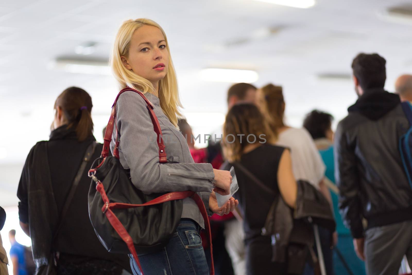 Young blond caucsian woman waiting in line with plain ticket in her hands. Lady standing in a long queue to board a plane.