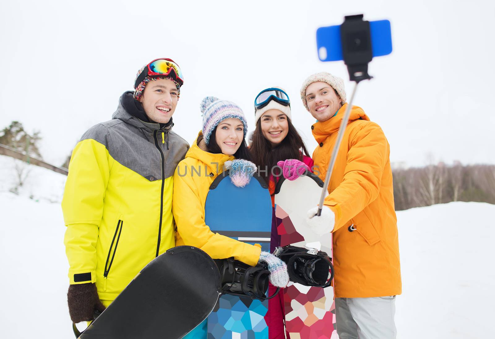 winter sport, leisure, friendship, technology and people concept - happy friends with snowboards and smartphone taking selfie