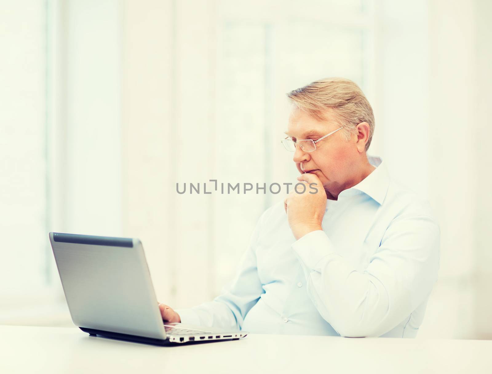 technology, oldness and lifestyle concept - old man in eyeglasses working with laptop computer at home