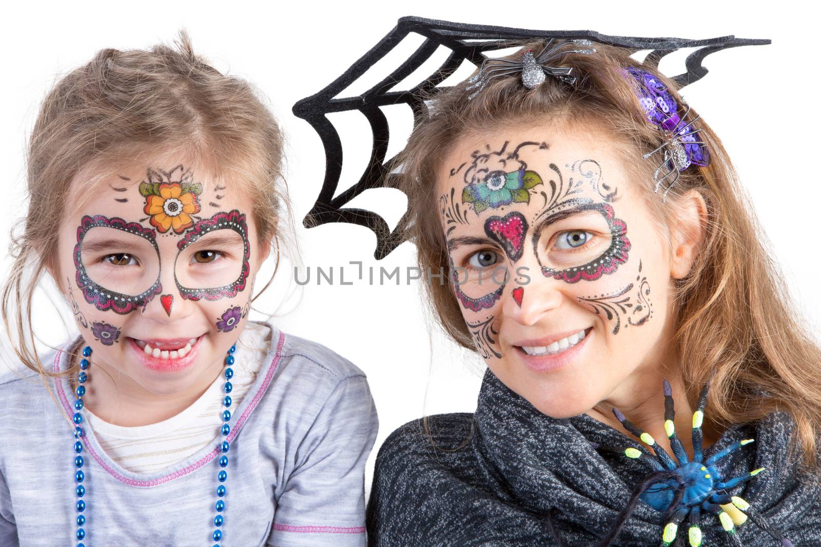 Pretty woman and her cute young daughter in Halloween makeup wearing a spider and its web looking at the camera with happy playful smiles, head and shoulders portrait over white