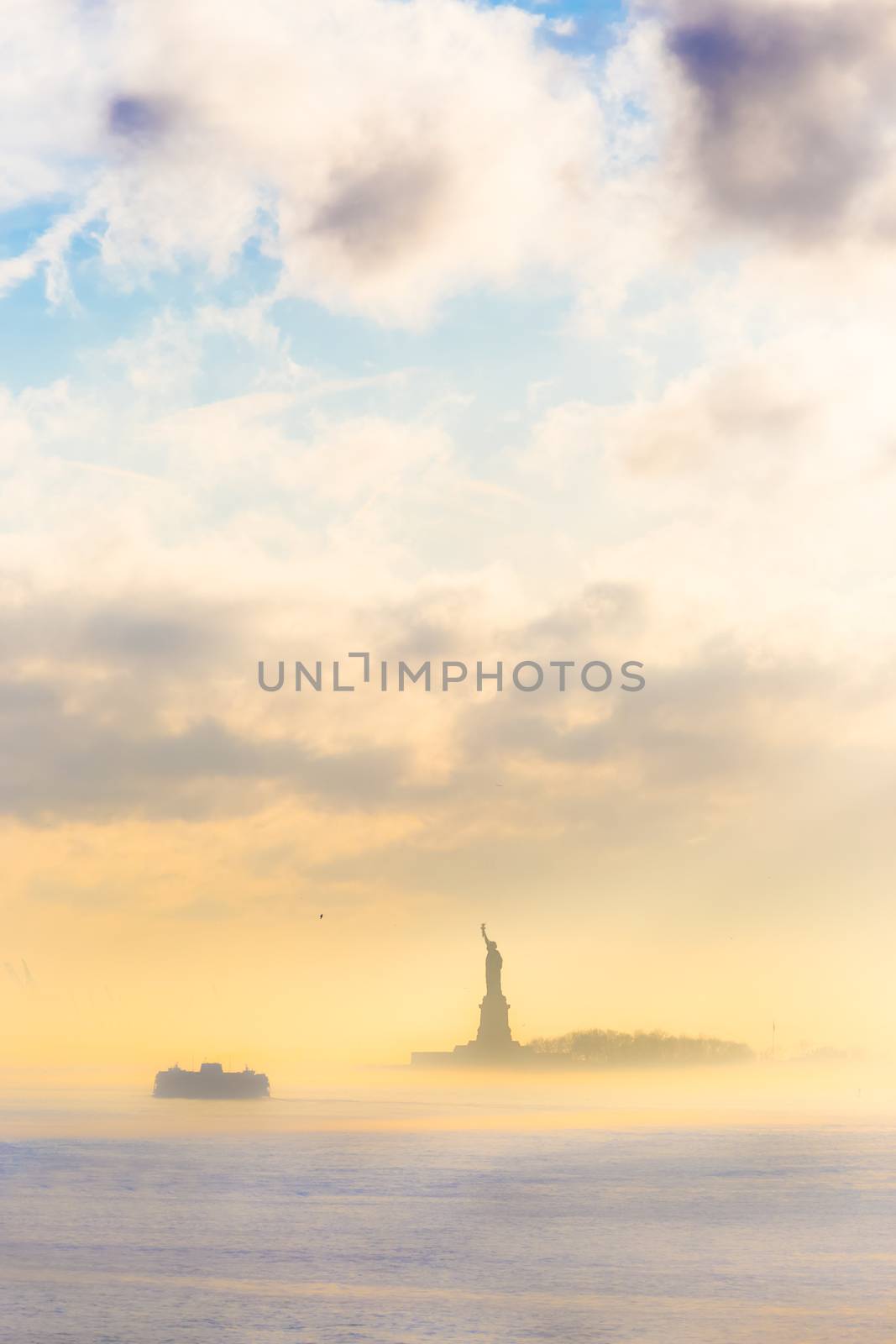 Staten Island Ferry cruises past the Statue of Liberty on a misty sunset. Manhattan, New York City, United States of America. Vertical composition. Copy space.