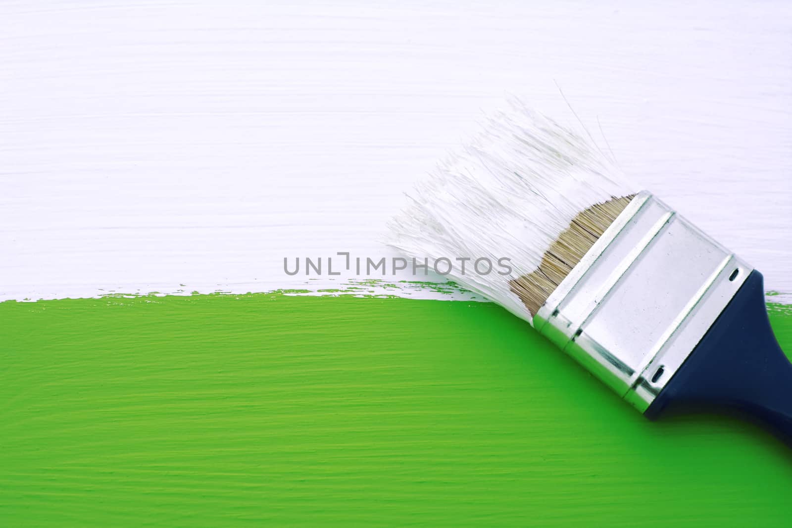 Painting green wooden surface with white paint, dirty paintbrush lies on top