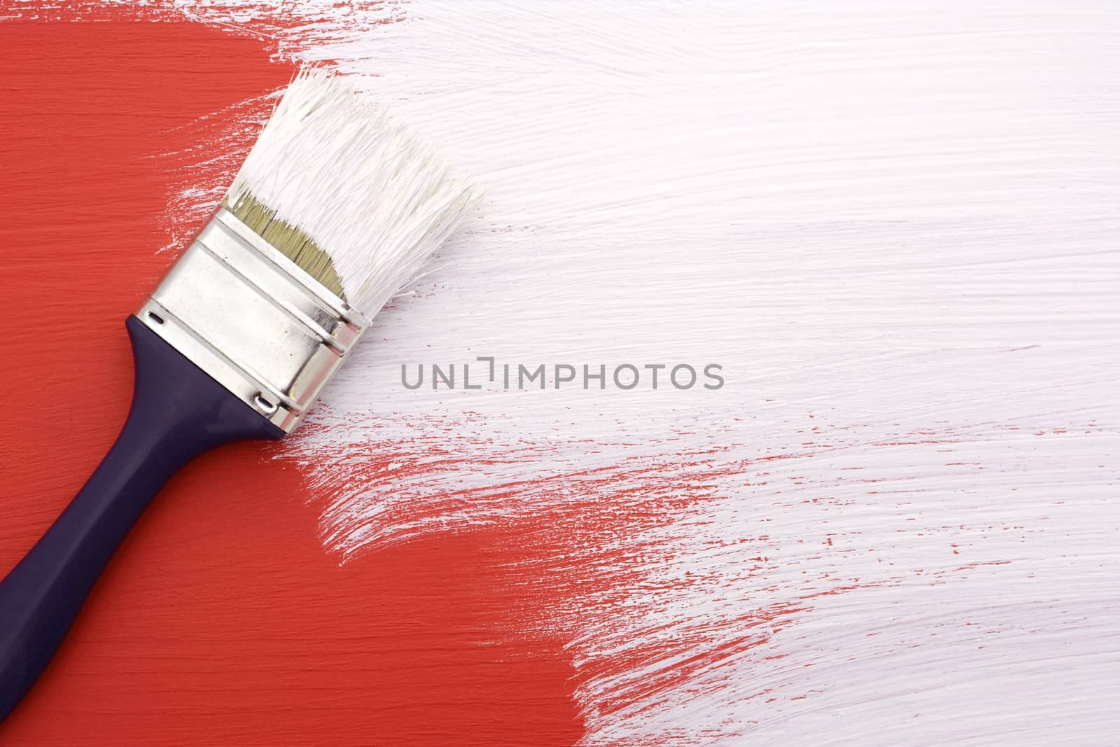 Paintbrush with white paint painting over red colour on a pine board