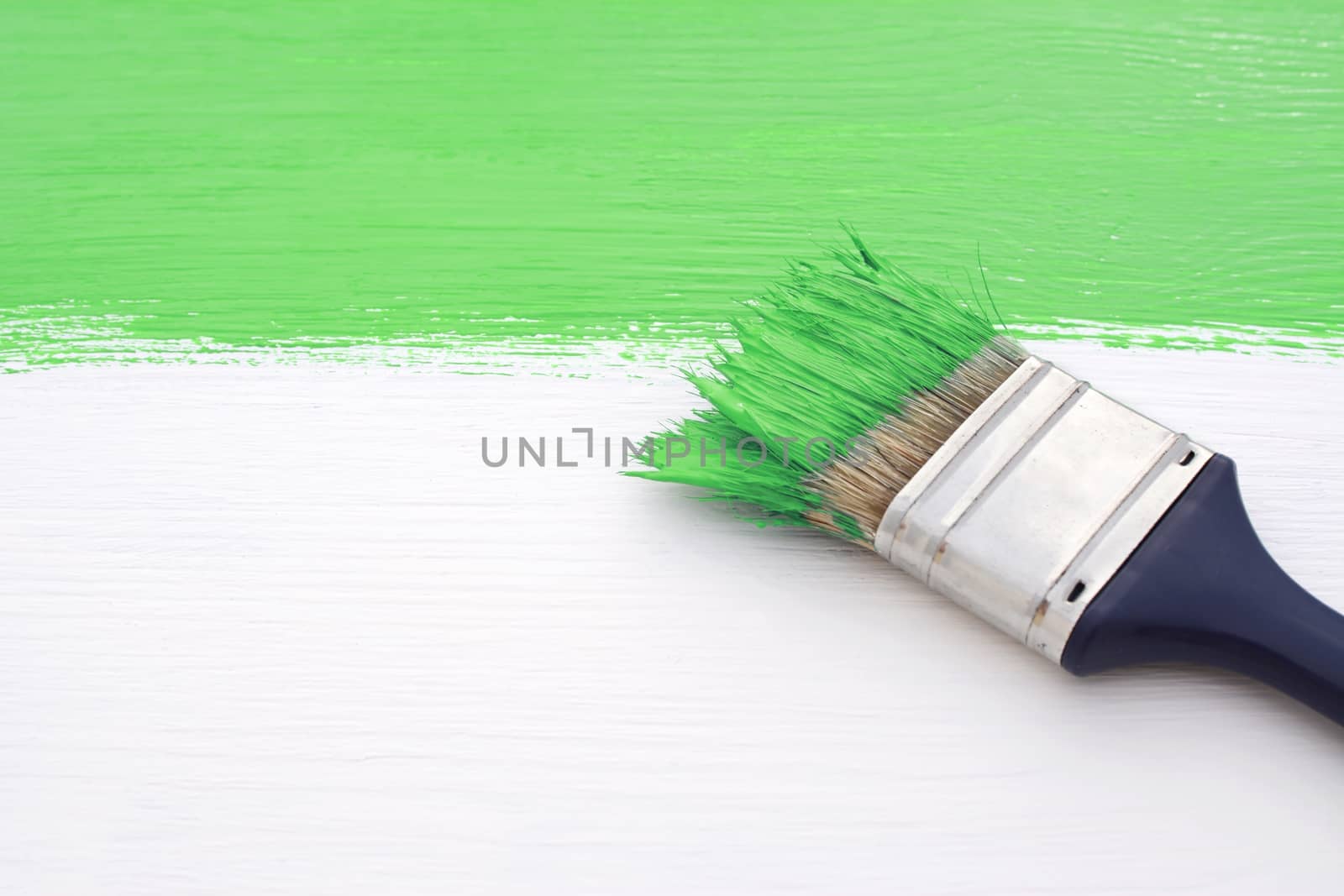 Paintbrush loaded with green paint, painting over white wooden board