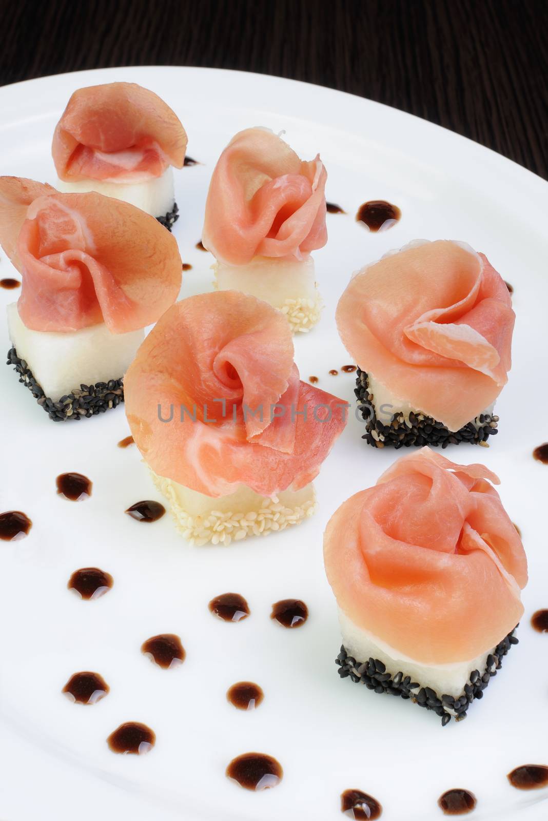 Appetizer of melon cubes in sesame with a slice of gammon