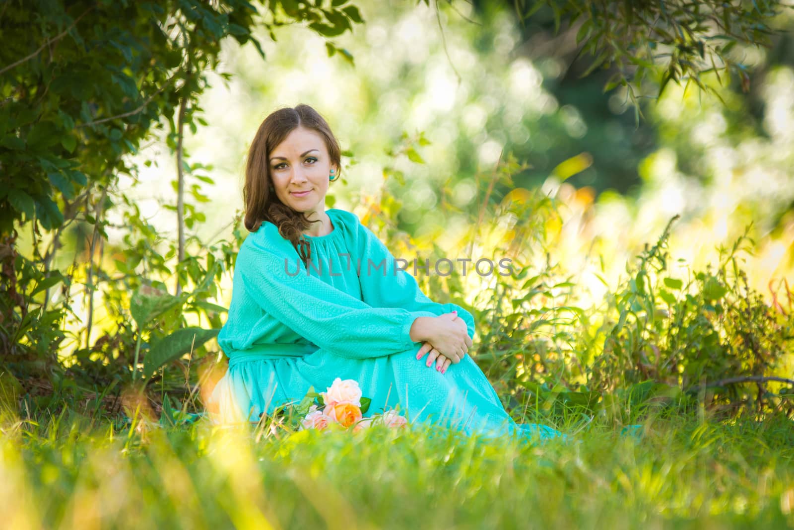 A girl in a long dress sitting on the grass in the forest in sunny weather by Madhourse