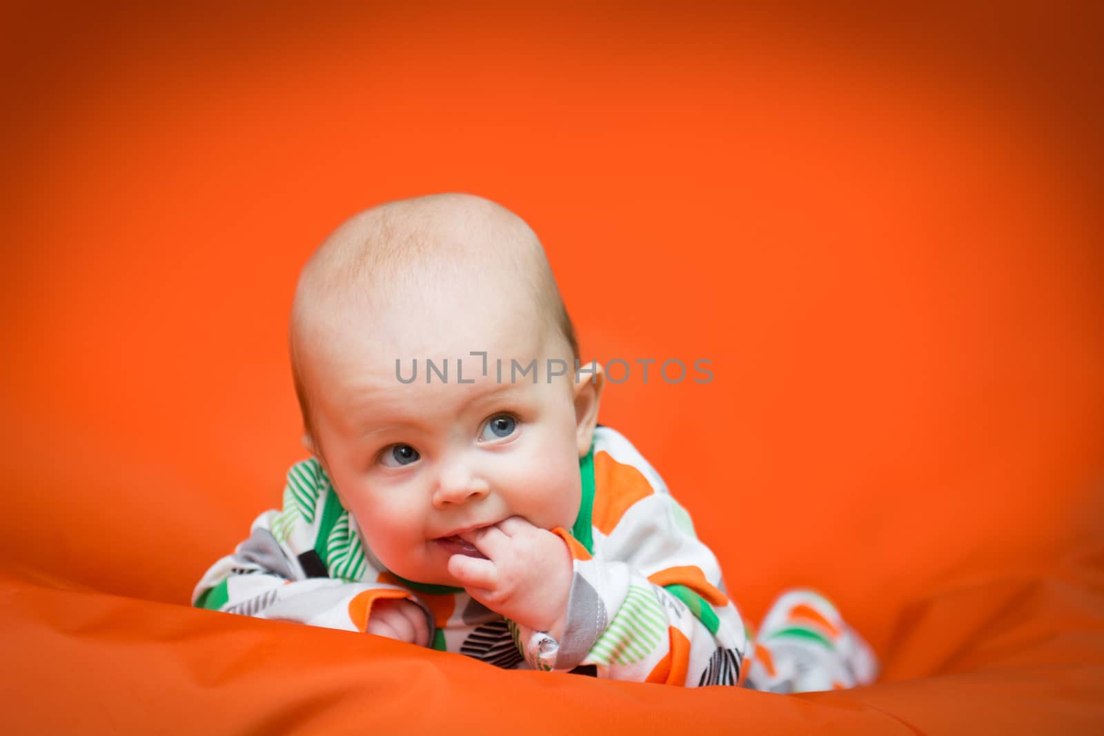 Baby girl lying on a belly on an orange pillow by kamsta