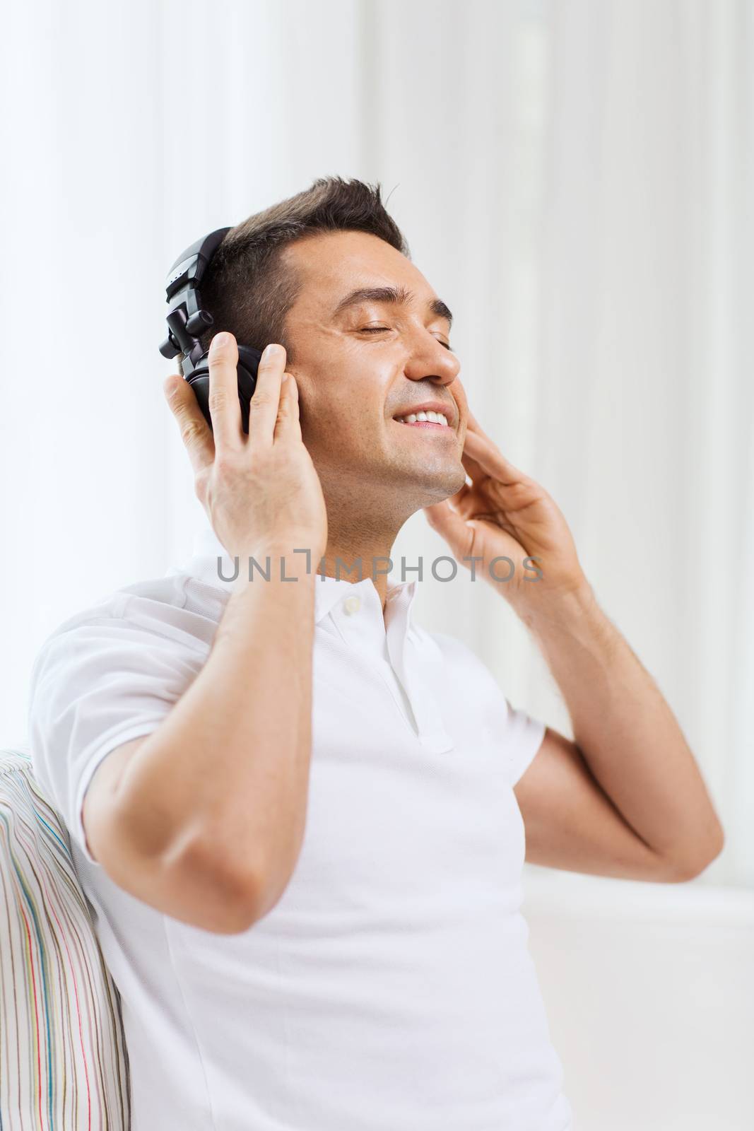 happy man in headphones listening to music at home by dolgachov
