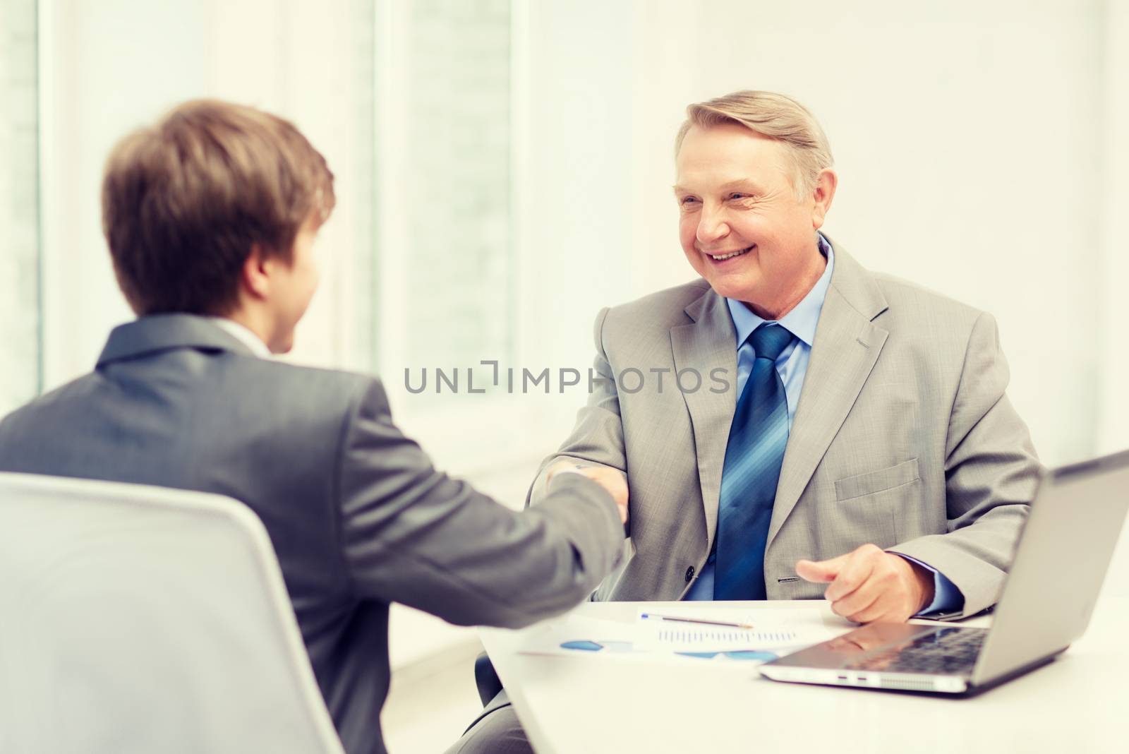 older man and young man shaking hands in office by dolgachov