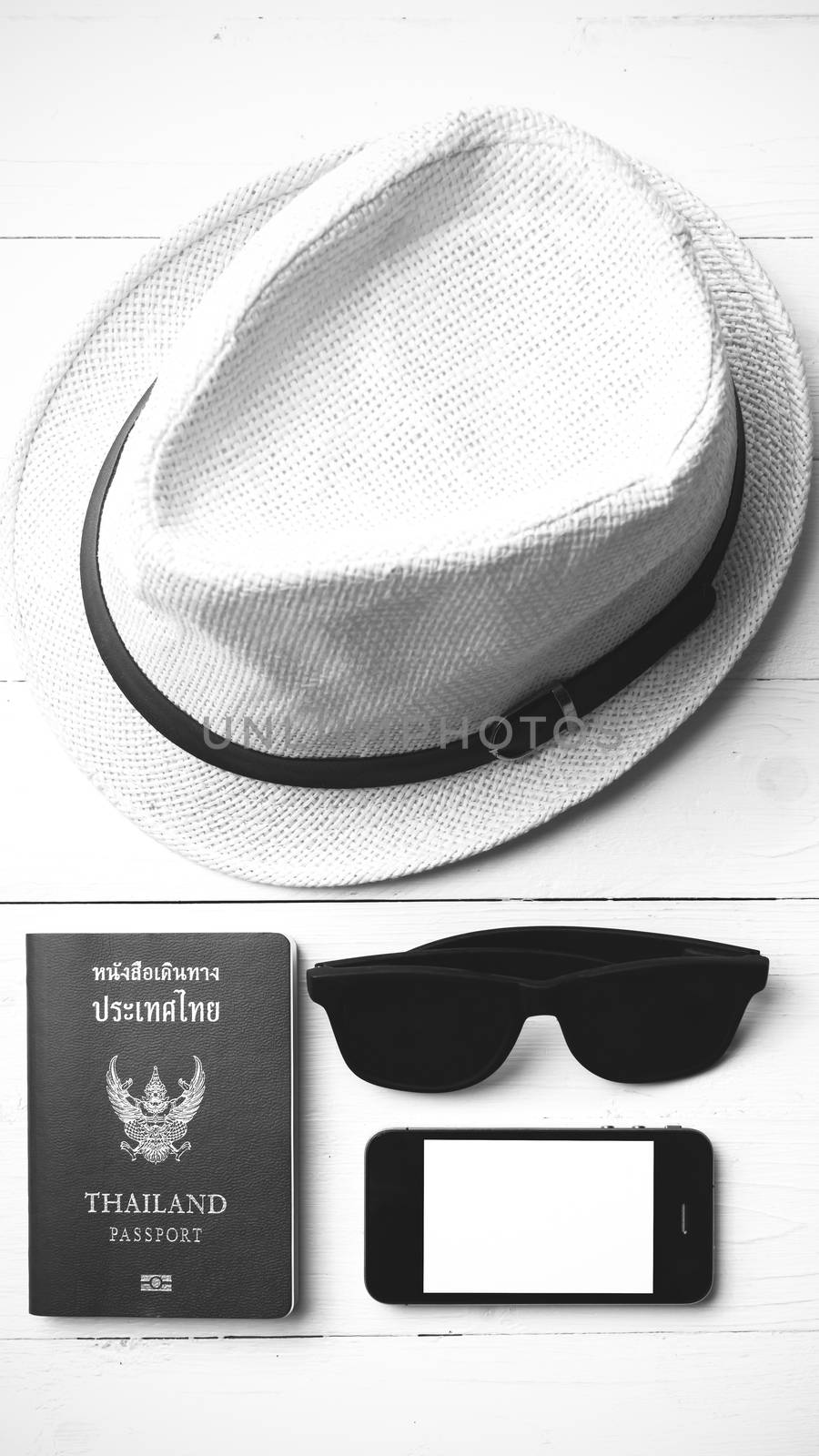 hat sunglasses smart phone and passport over white table black and white color
