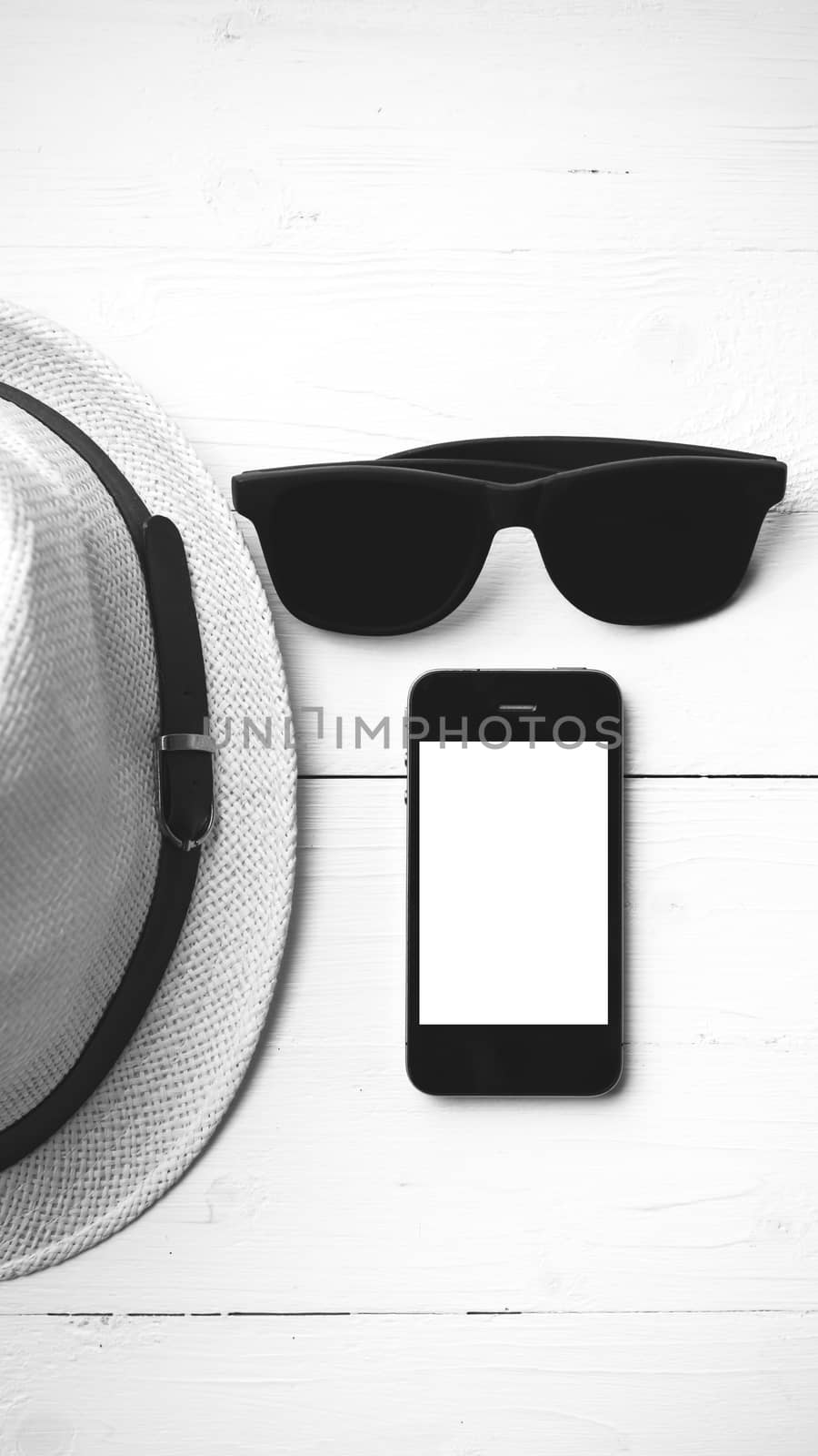 hat sunglasses and smart phone on white table black and white color