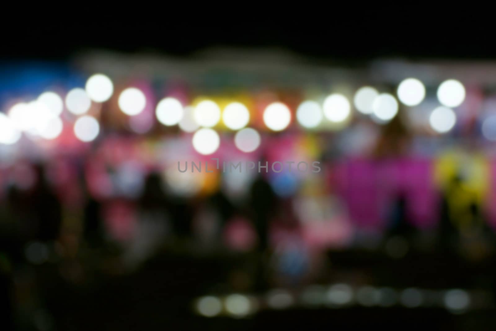 Defocused and blurred image of people at amusement park at night for background usage.
