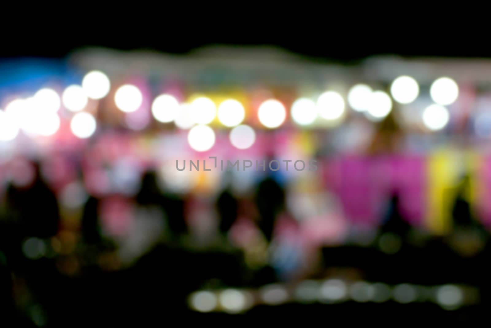 Defocused and blurred image of people at amusement park at night for background usage.