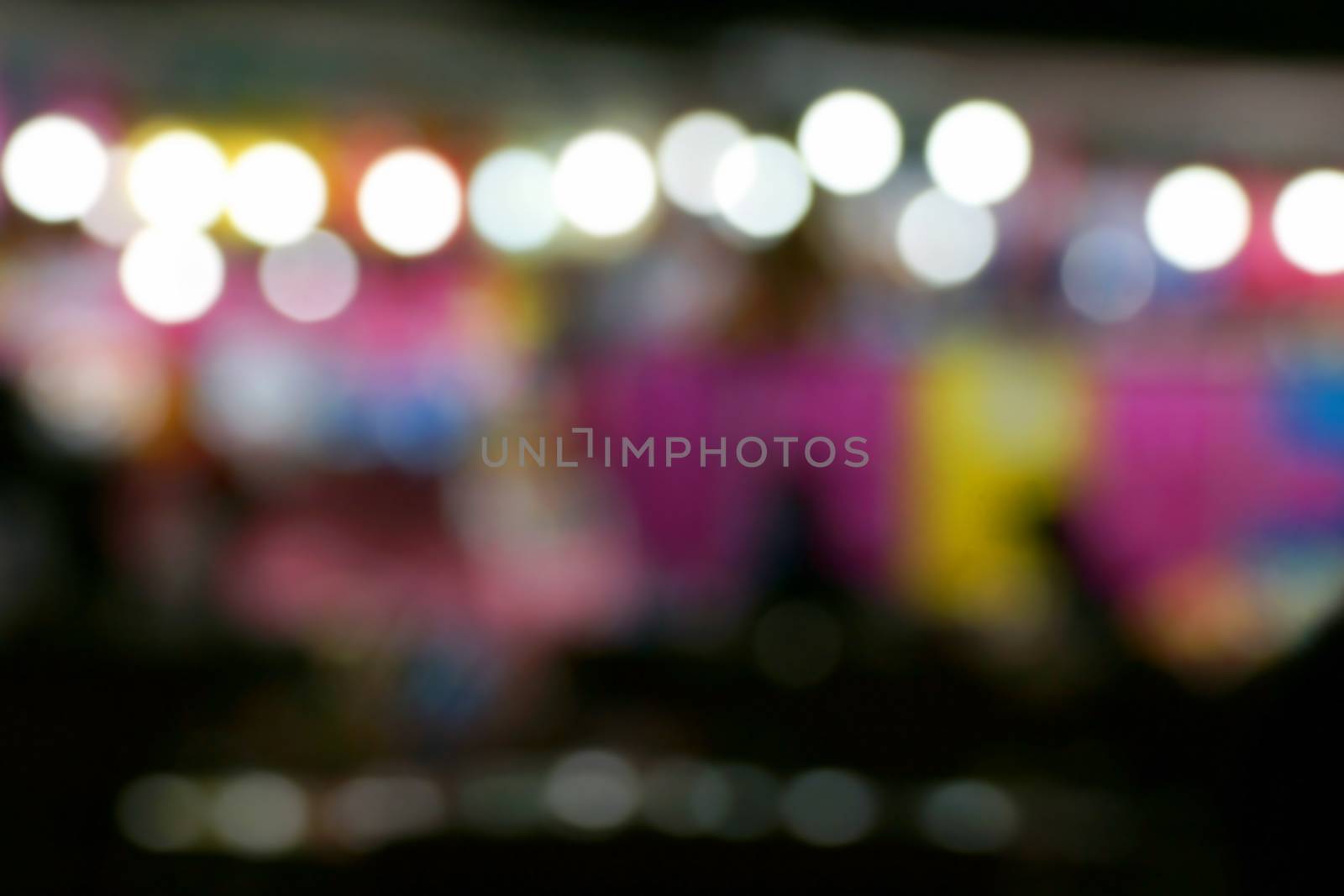 Defocused and blurred image of people at amusement park at night for background usage.