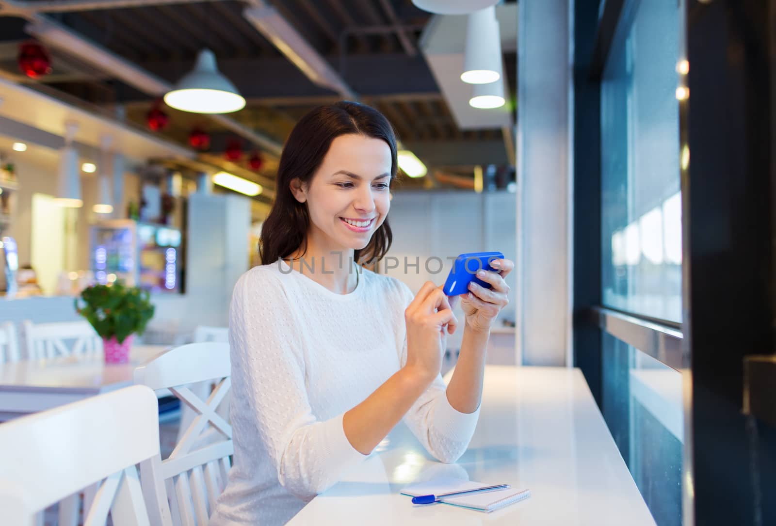 business, people, technology and lifestyle concept - smiling young woman texting message with smartphone at cafe